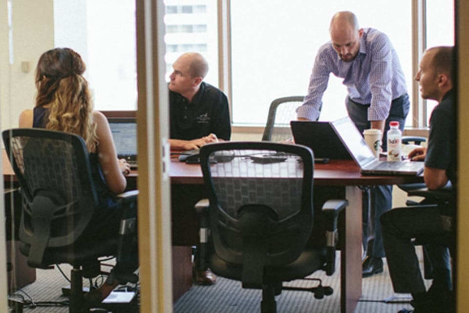 Four professionals in a modern office meeting, collaborating around a conference table.