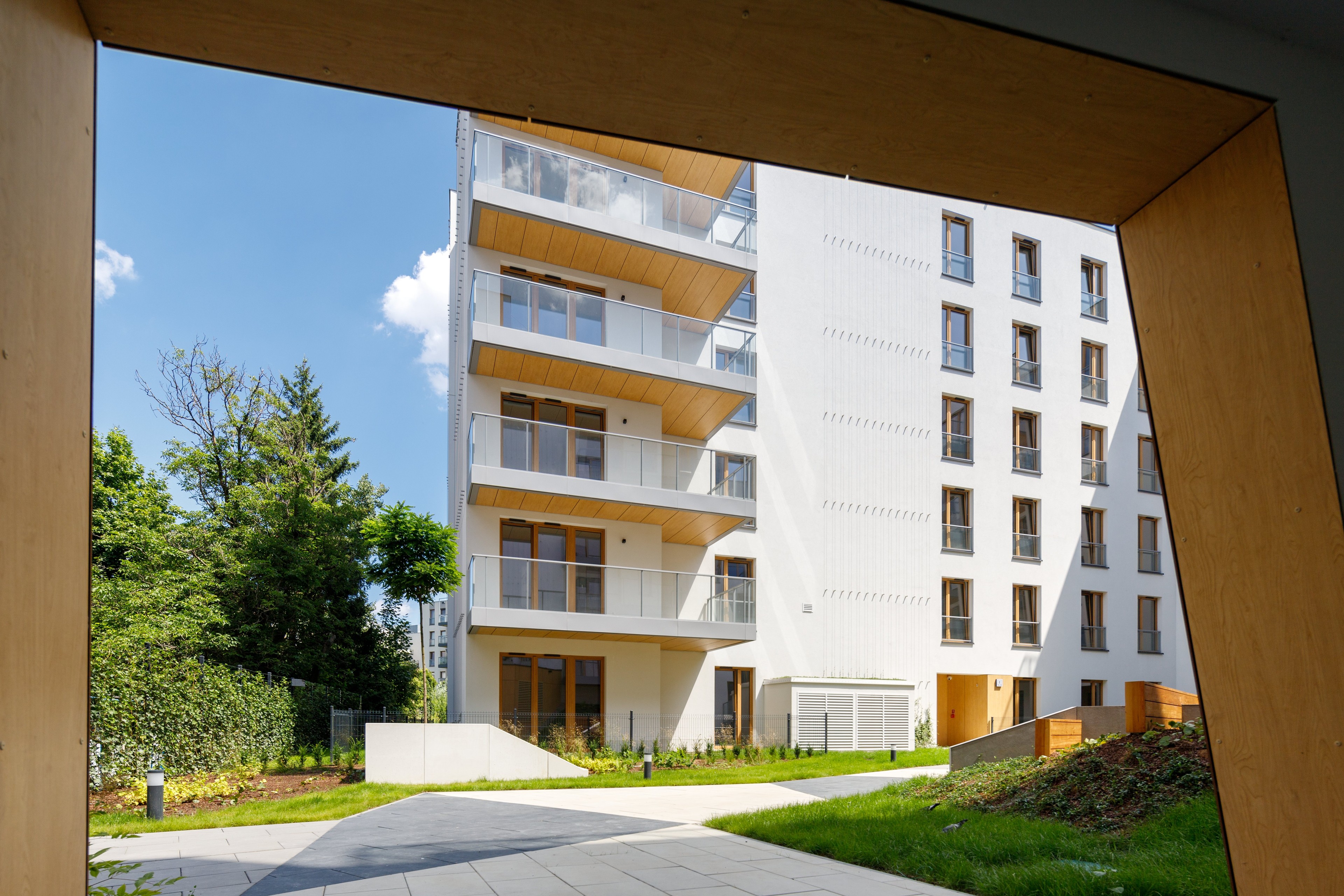 Nowoczesny budynek apartamentowy z balkonami, otoczony zielenią, pod czystym niebieskim niebem.