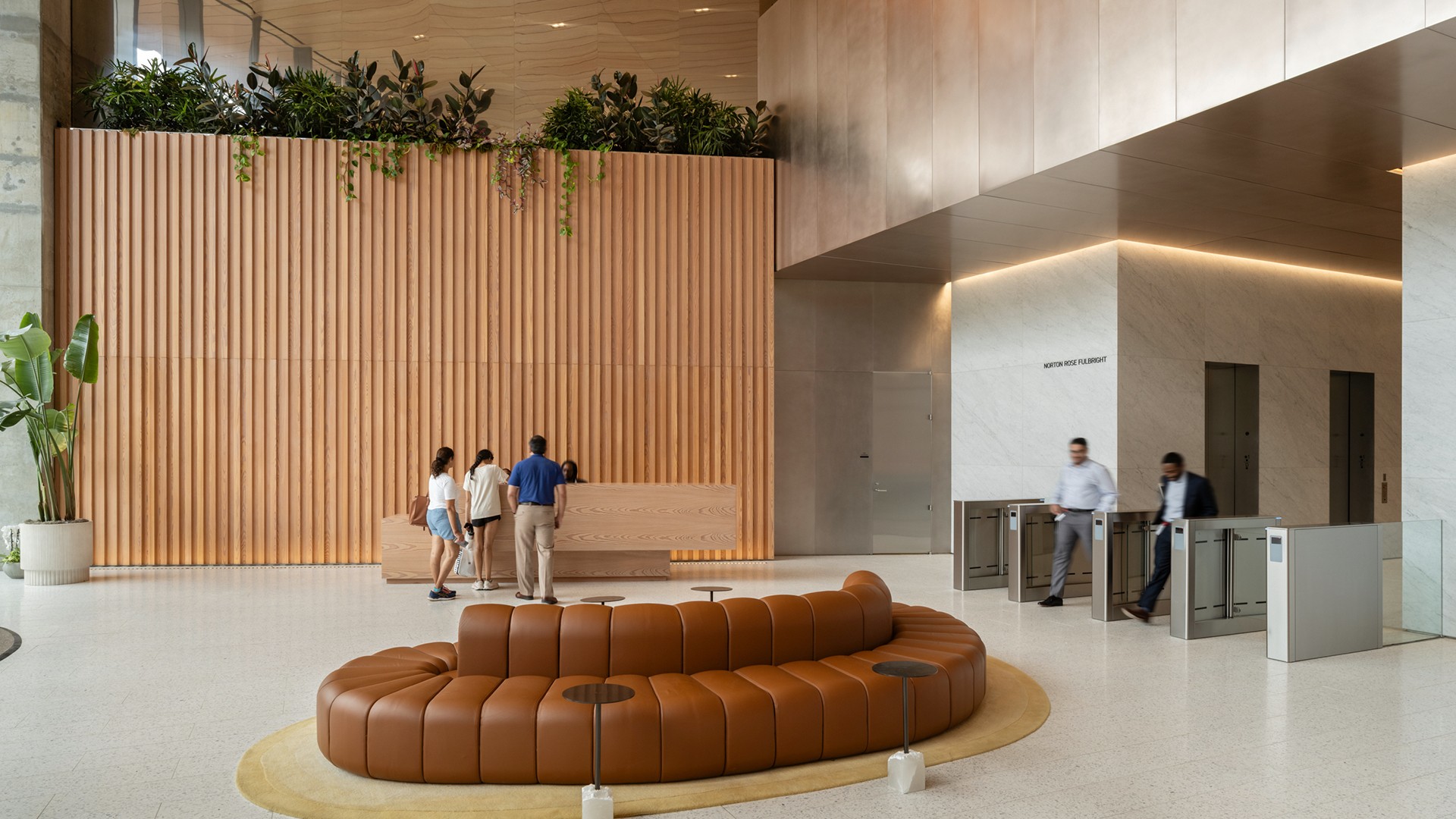 Modern office lobby with curved brown seating, wooden wall, and people at reception.