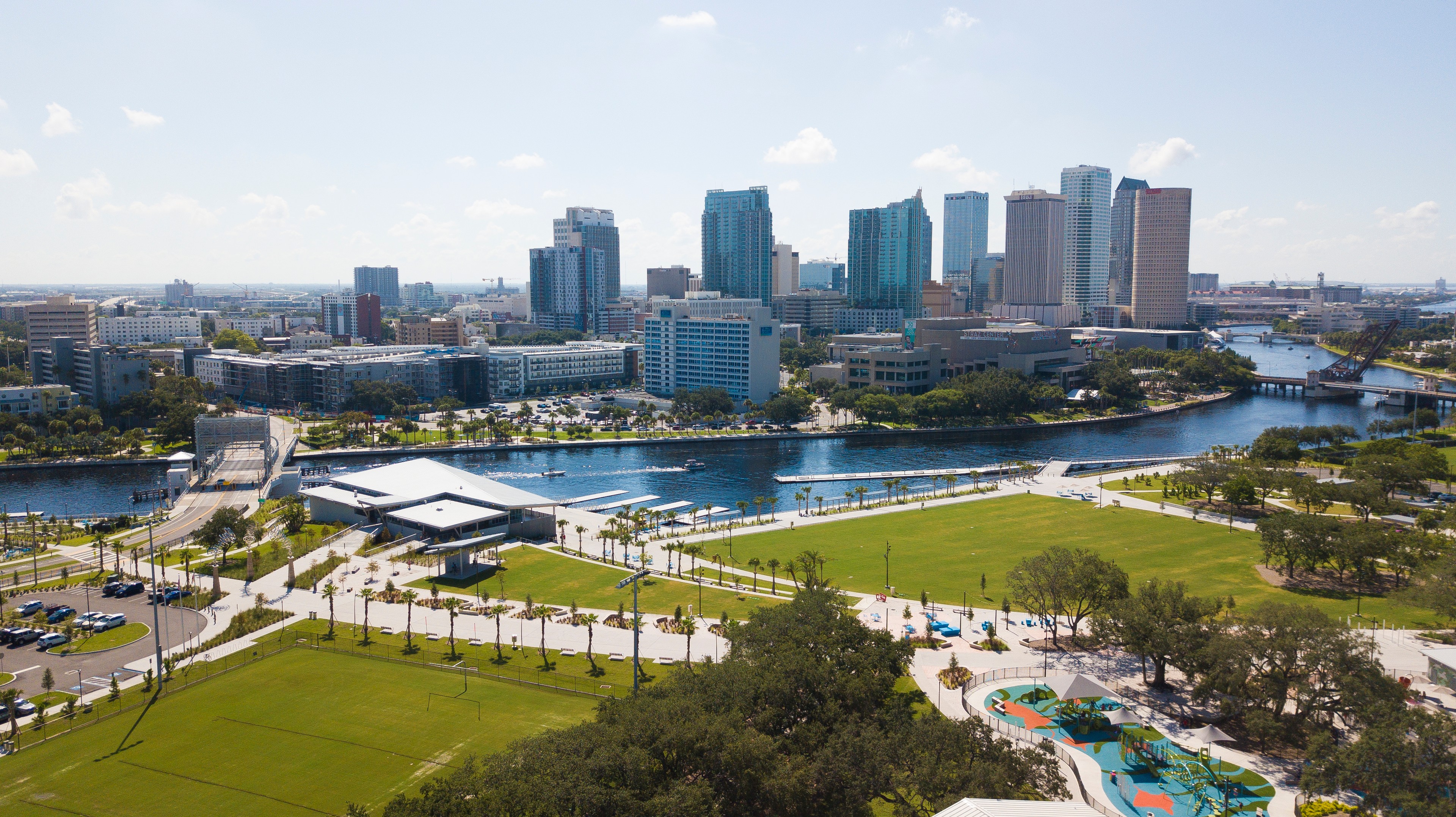 Urban Park Design: Aerial View of Landscaped Spaces Waterfront park with modern white benches, palm trees, and clear blue sky on a sunny day.