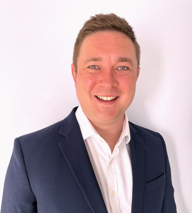 Professional Man in Suit Against White Background A person in a dark suit and white shirt stands against a plain white background.