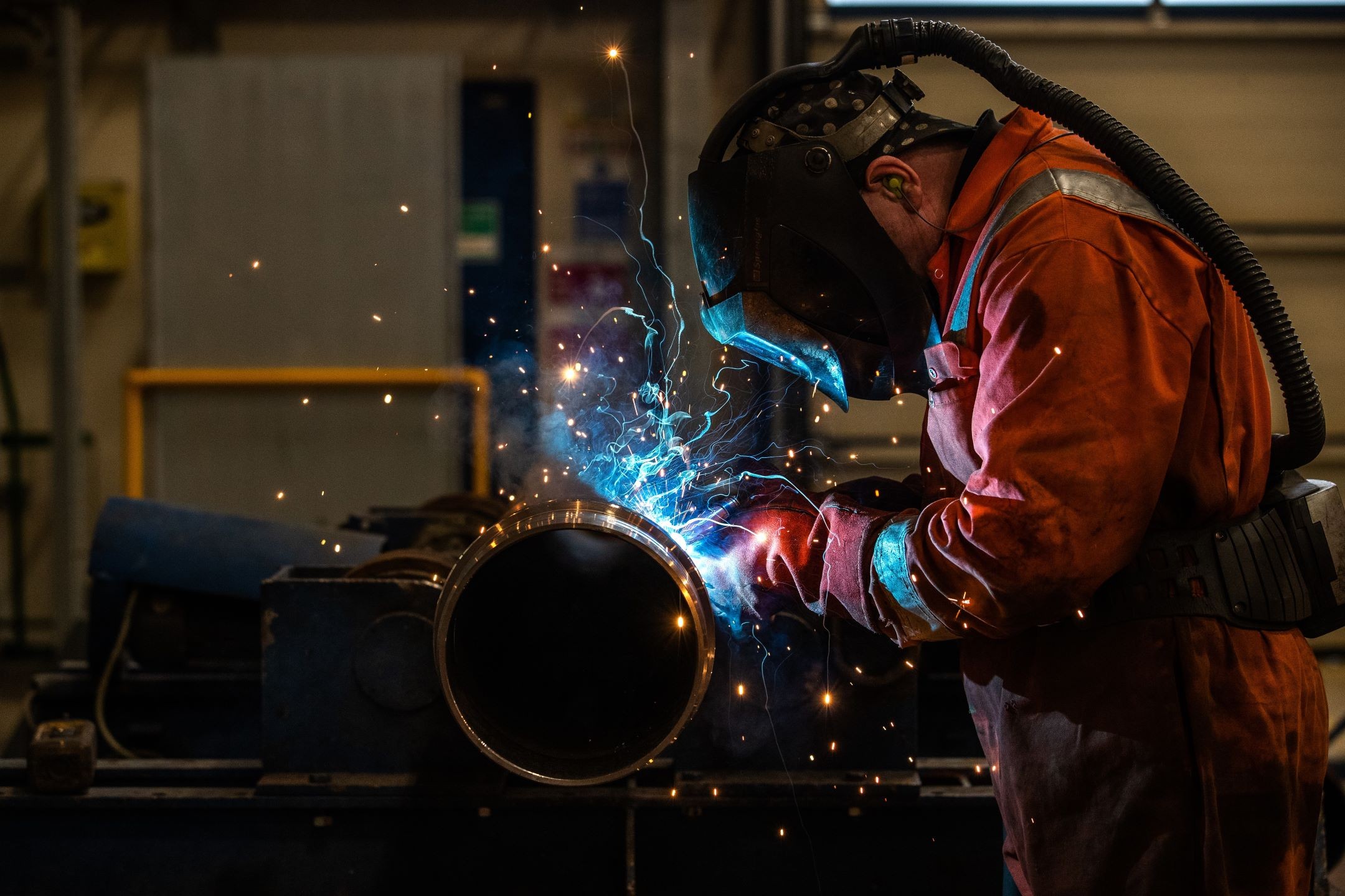 Welder at Work Creating Sparks in Industrial Workshop Welder in protective gear welding a metal pipe with bright sparks in a workshop.