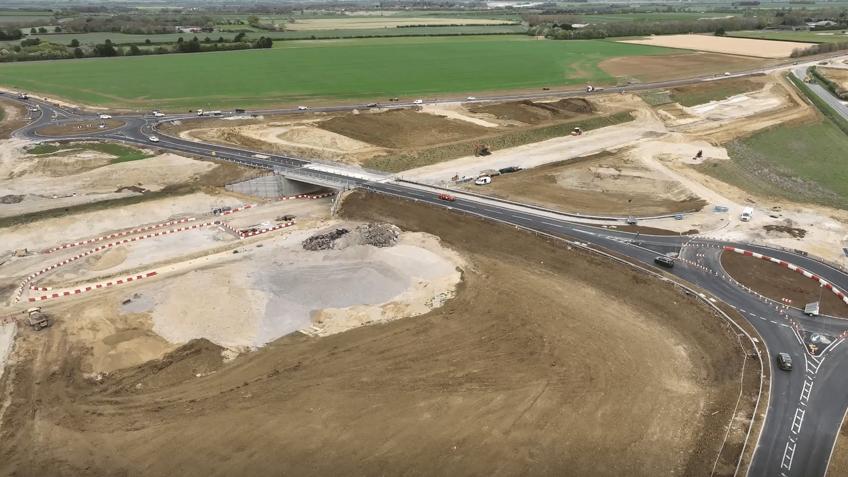 Aerial view of a highway construction site with new roads and green fields in the background.