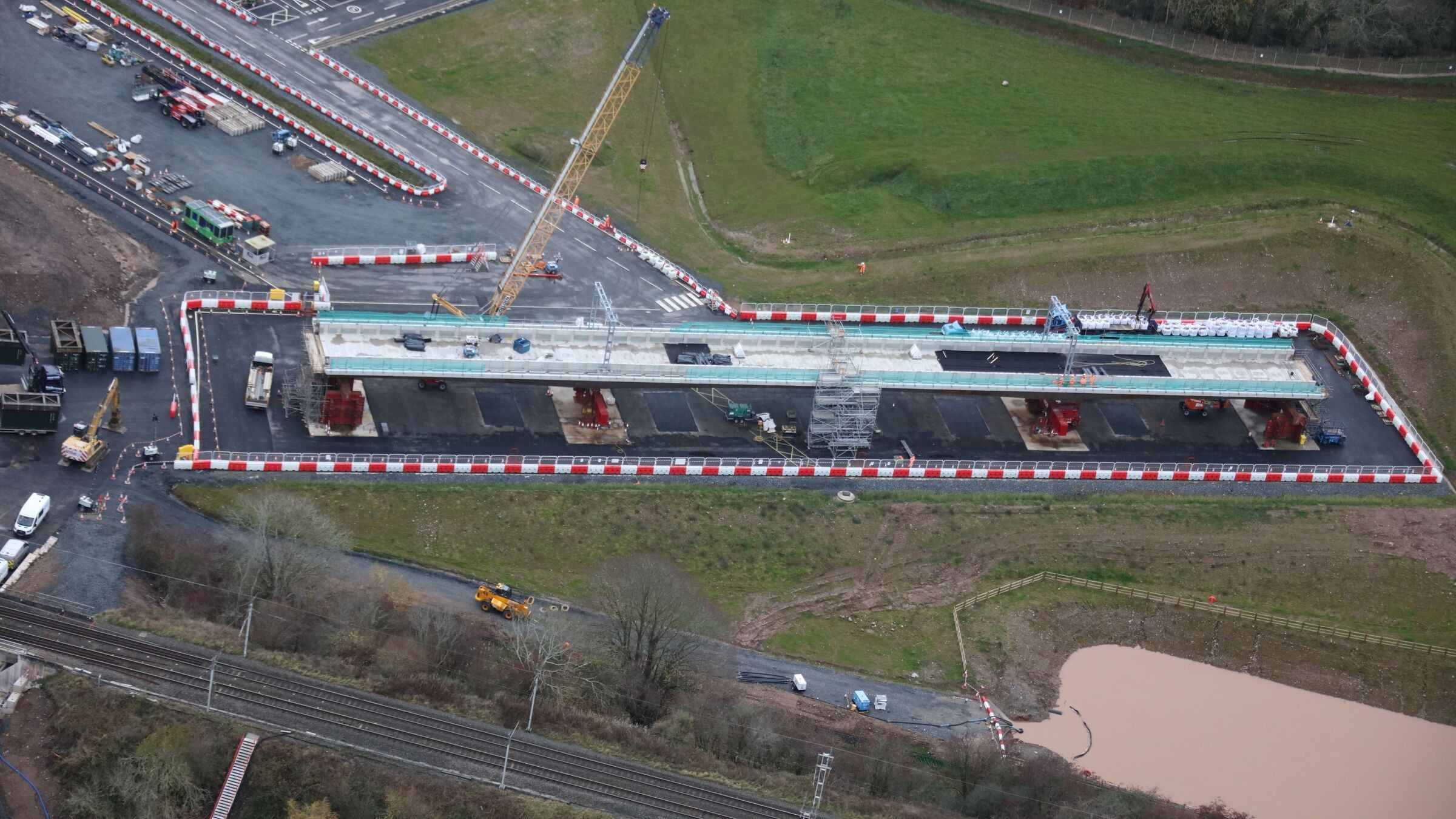Aerial view of an under-construction bridge with cranes and construction vehicles.
