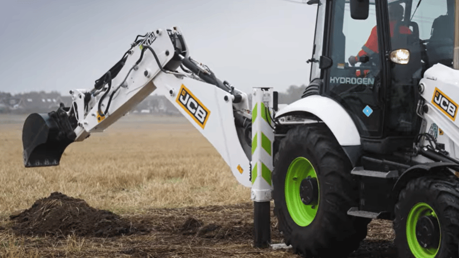 White JCB excavator with green wheels digging soil in a field, hydrogen powered.