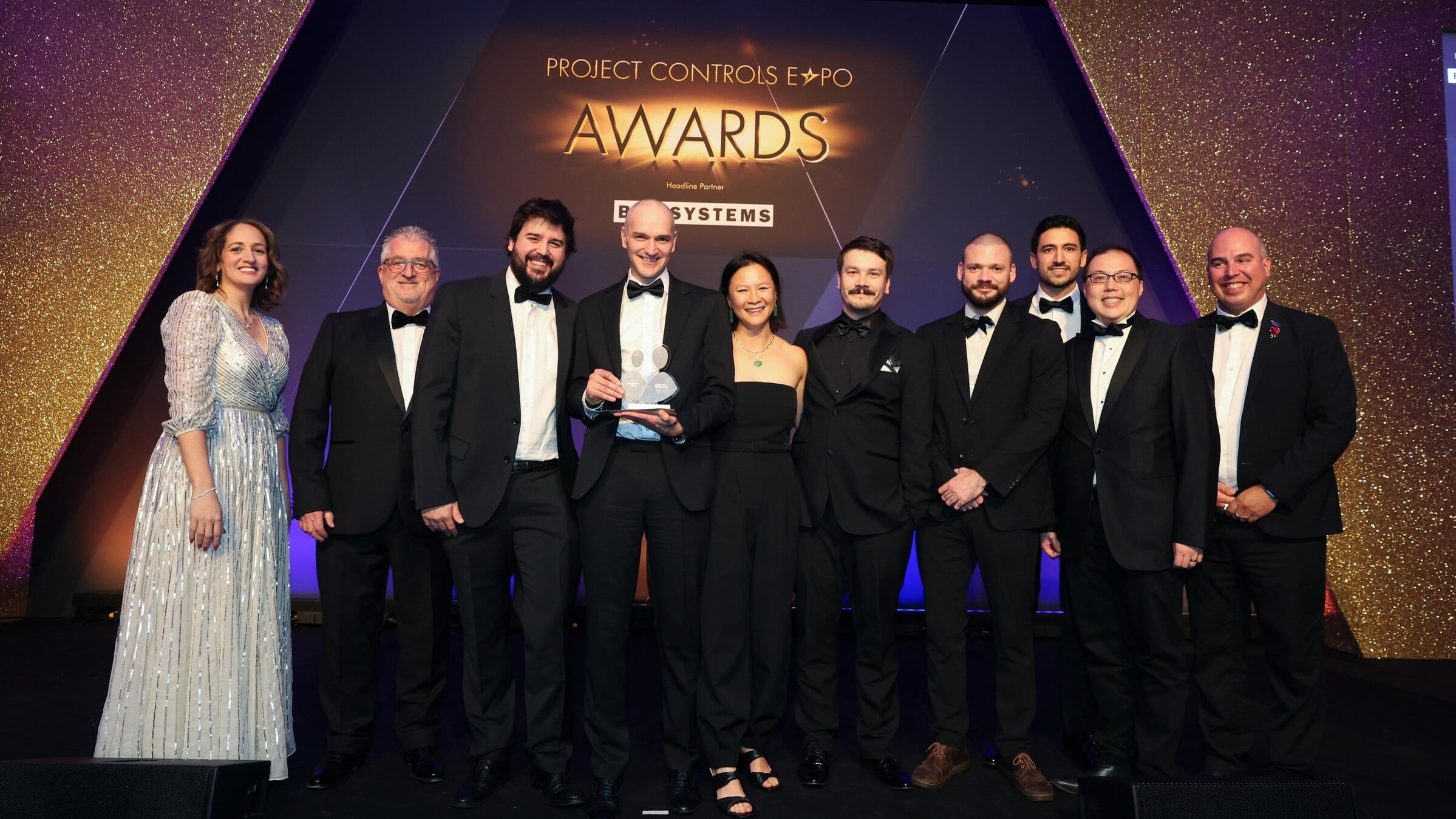 Group of formally dressed professionals posing on stage at Project Controls Expo Awards event.