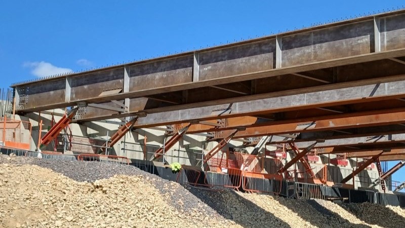 Steel beams and supports under construction at a large bridge site with gravel piles.