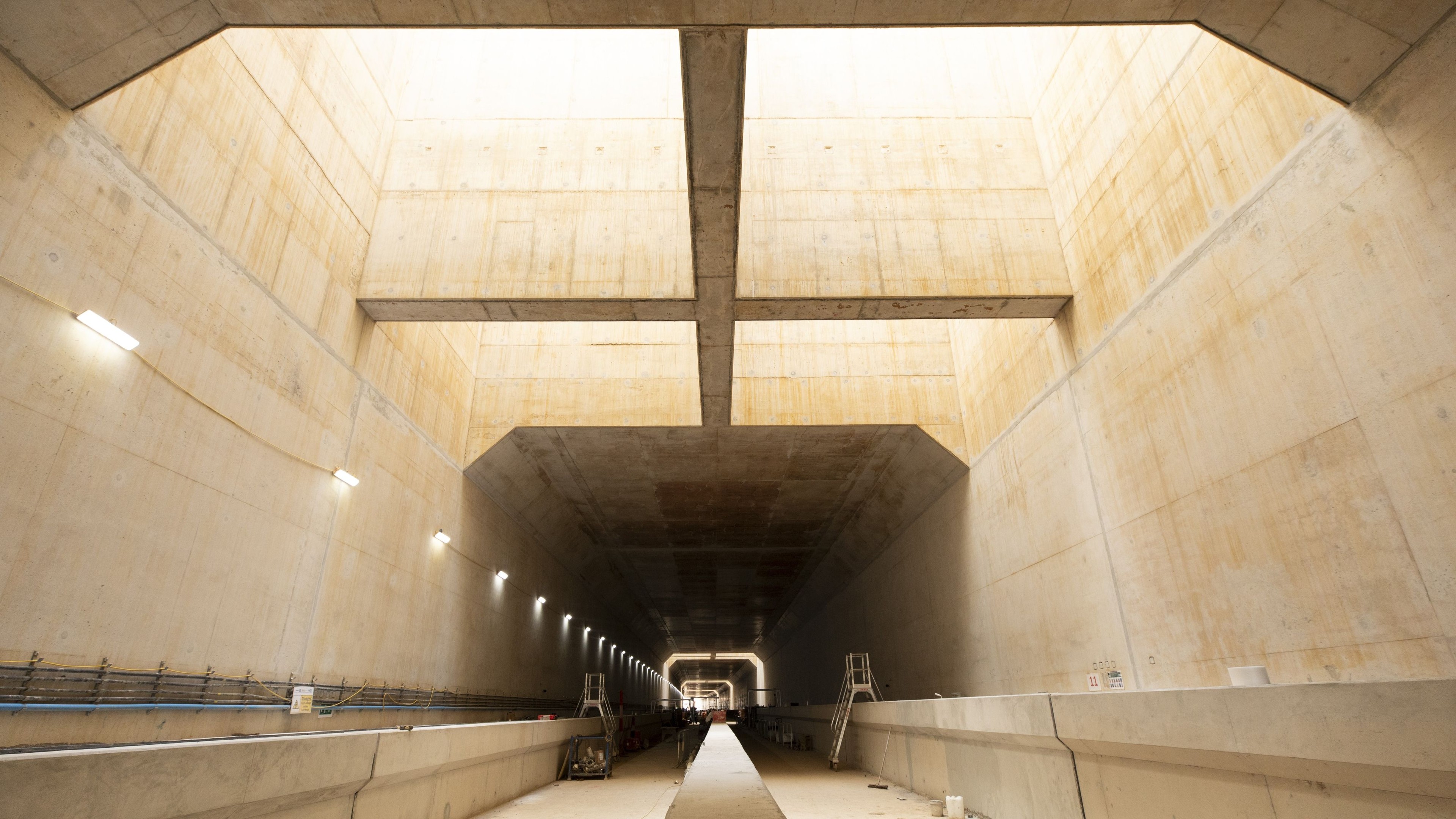 Interior view of a large, well-lit concrete tunnel under construction with open ceiling.