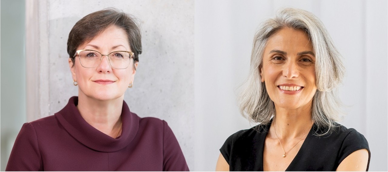 Two professional women, one with glasses and short brown hair, the other with gray hair, smiling.