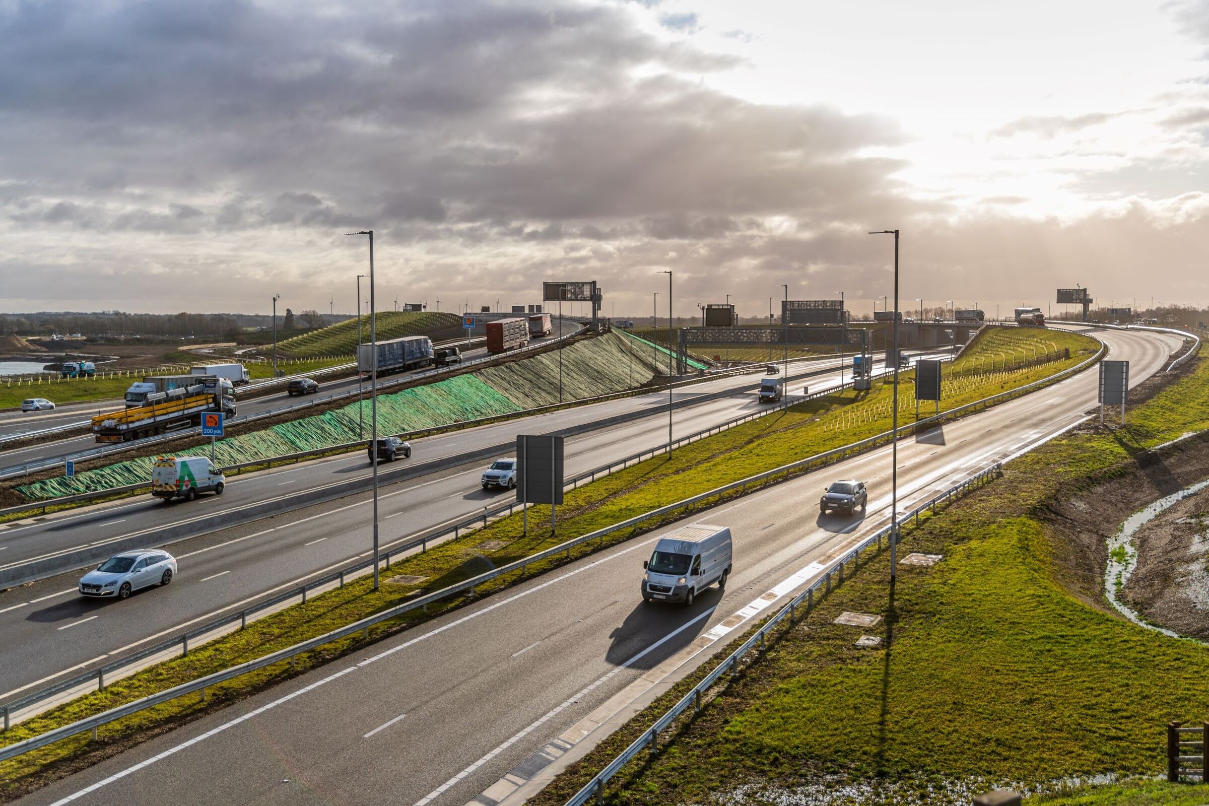 Modern Highway: Efficient Transportation Infrastructure Sunny highway scene with various vehicles, green slopes, and dramatic clouded sky.