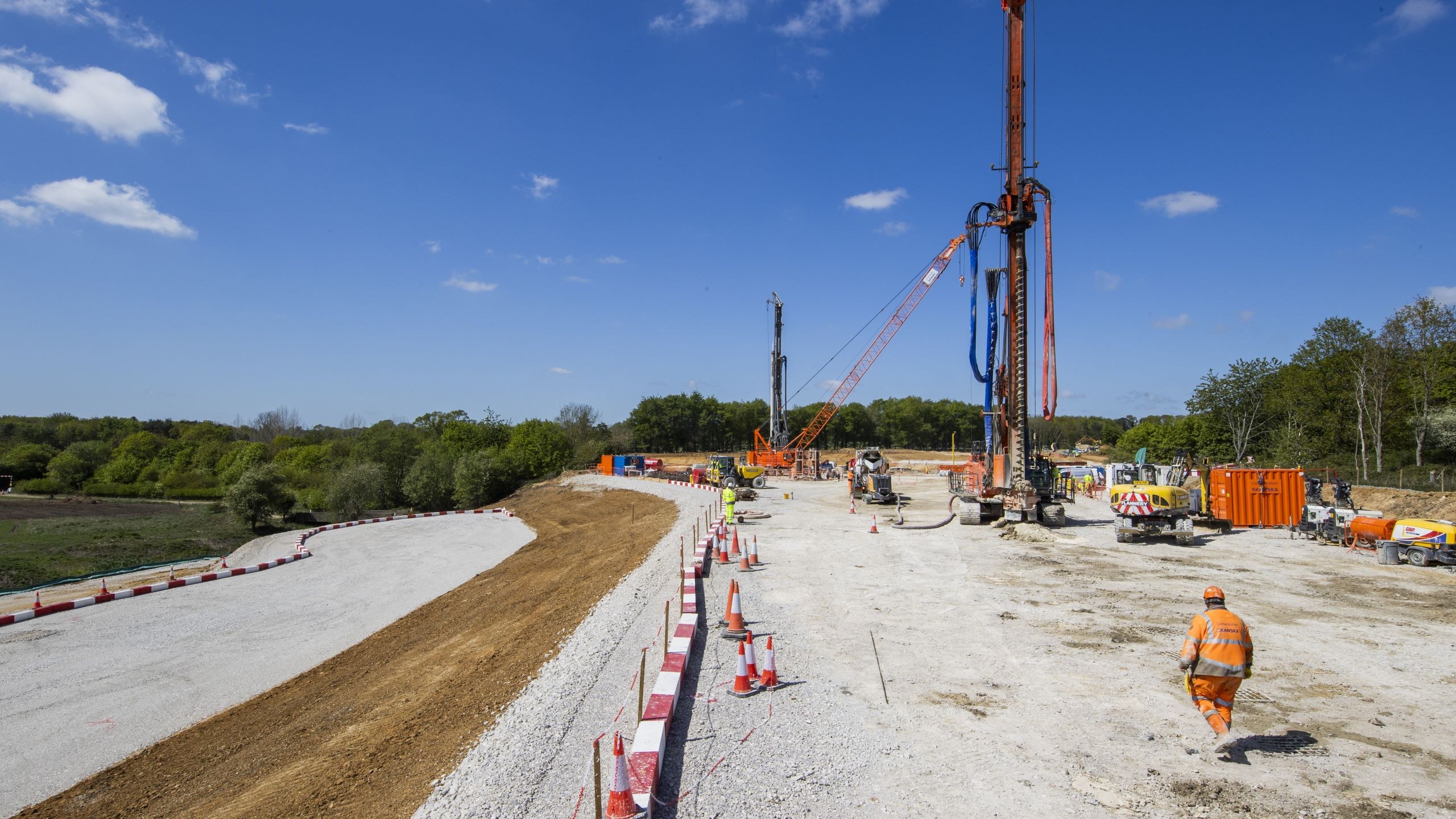 Construction site with heavy machinery and workers building a road under clear sky.