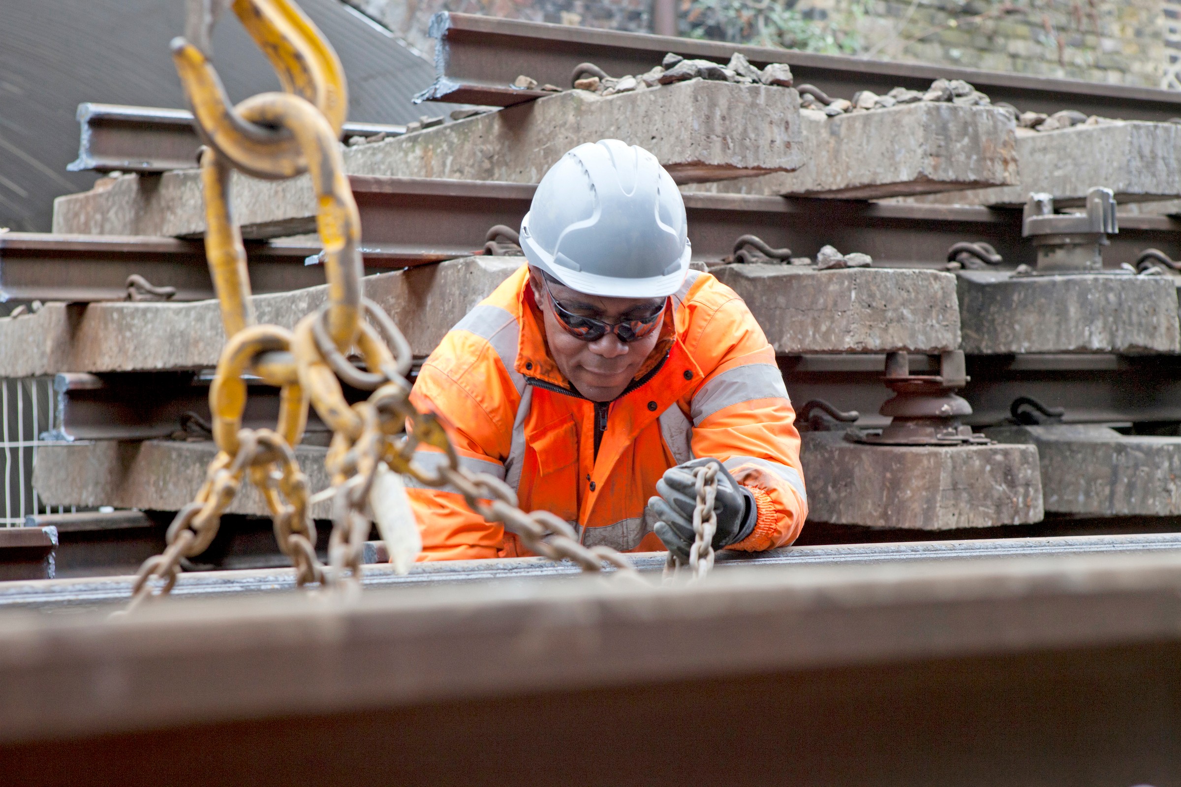 Railway Construction Worker in Safety Gear Handling Equipment Construction worker in high-visibility gear handling chains on a railway track site.