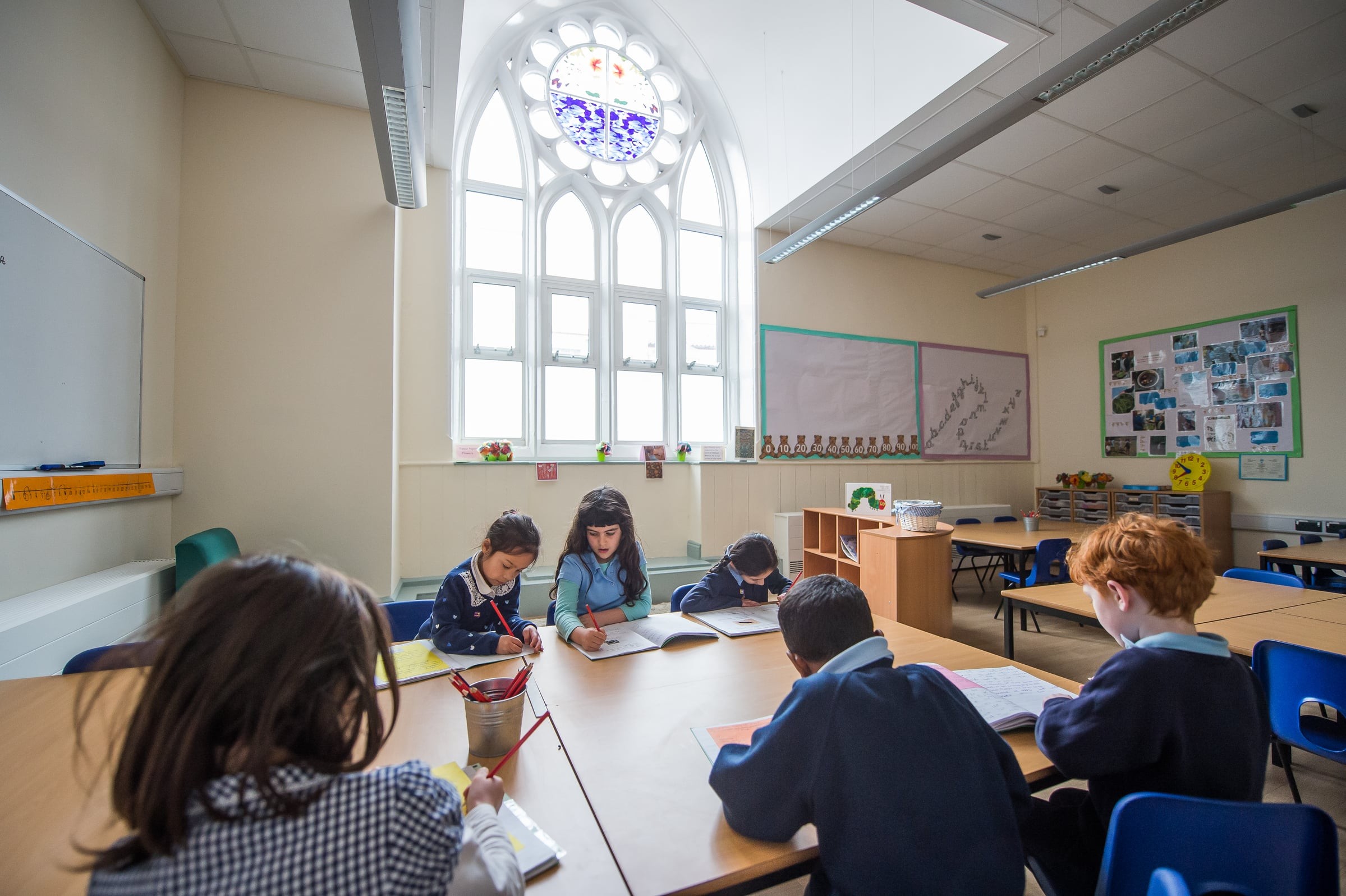 Children in a classroom with large windows and colorful educational displays on the walls.