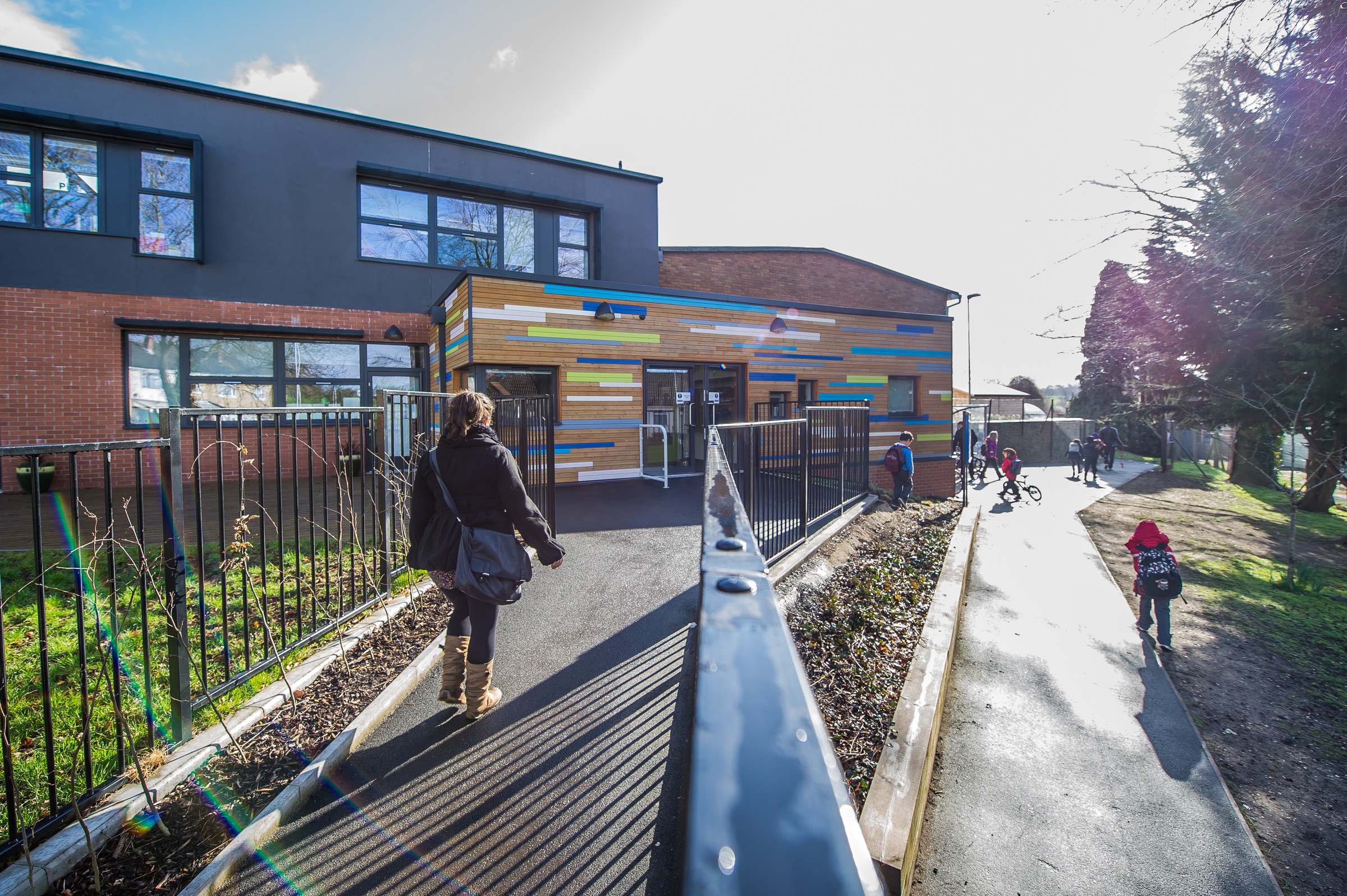 The colourful external façade at Glenfrome Primary Modern school entrance with colorful facade, people walking, and children riding bicycles.