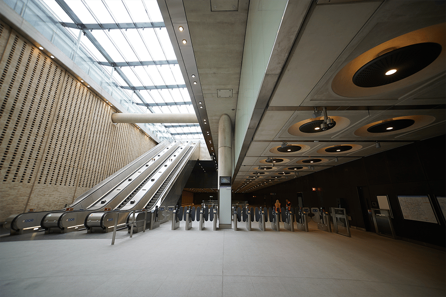 Modern subway entrance with escalators, ticket barriers, and skylight roof, featuring sleek design.