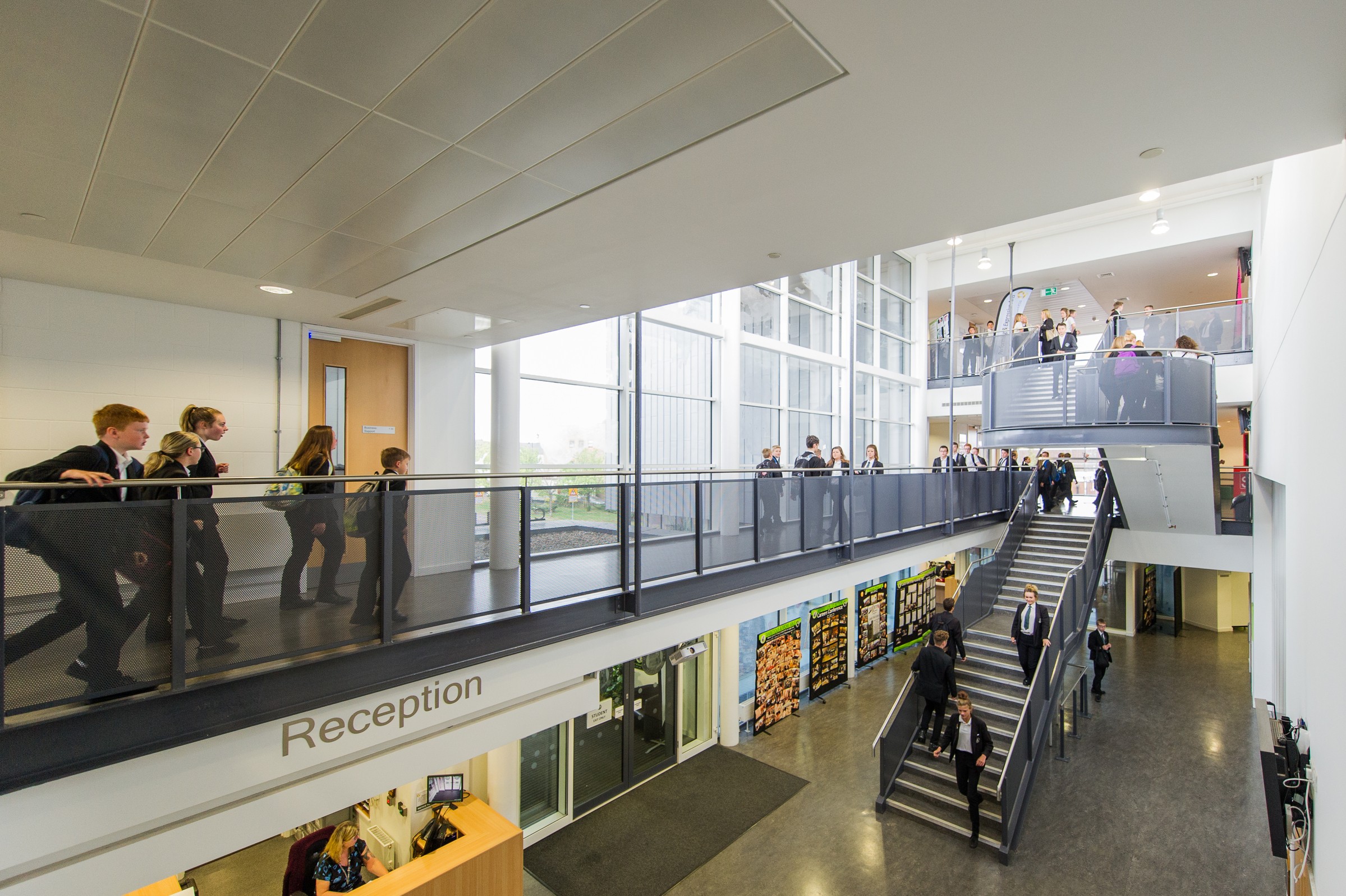 Modern school lobby with students on stairs and a reception area, featuring large windows.