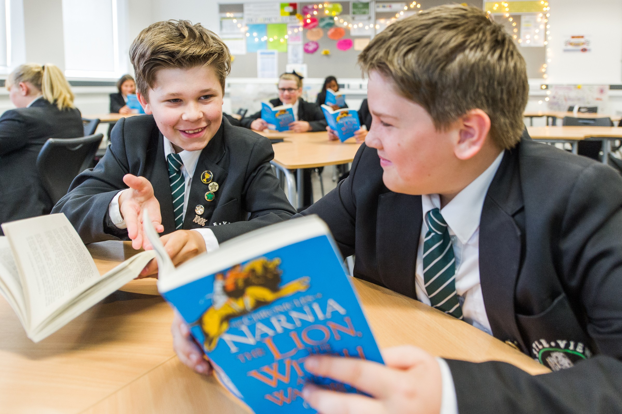 Students in a classroom read "The Lion, the Witch and the Wardrobe," wearing school uniforms.