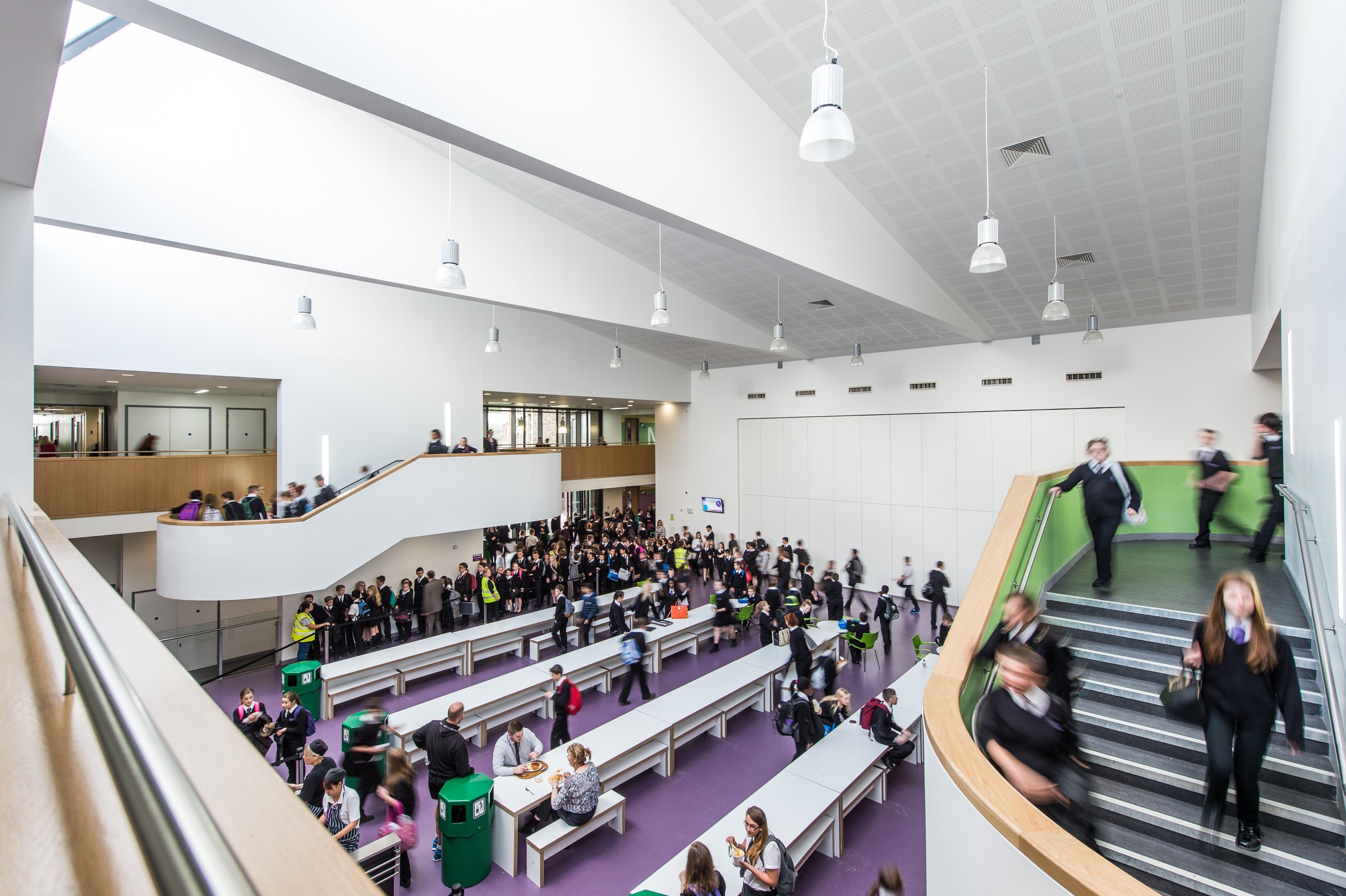 Essex Schools - Woodlands School Modern school cafeteria bustling with students in uniform, featuring white walls and long tables.