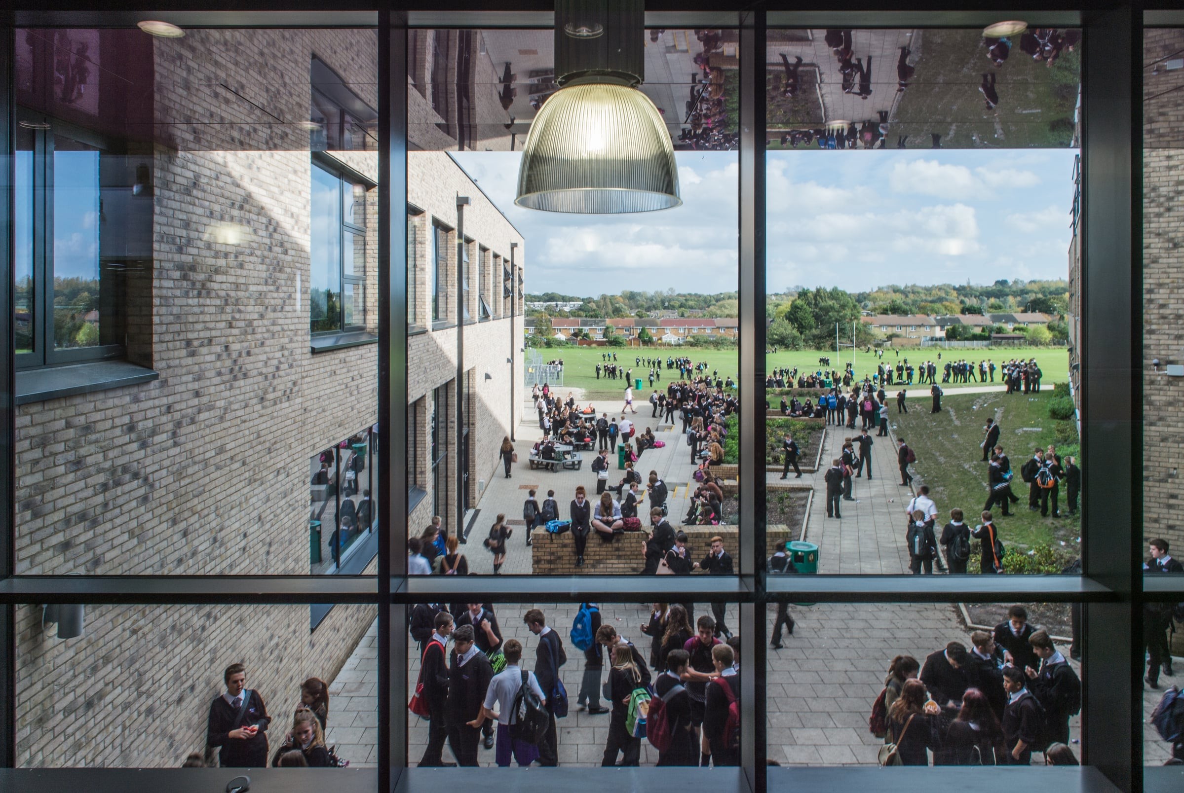 View through a window of a busy school courtyard filled with students during a break.