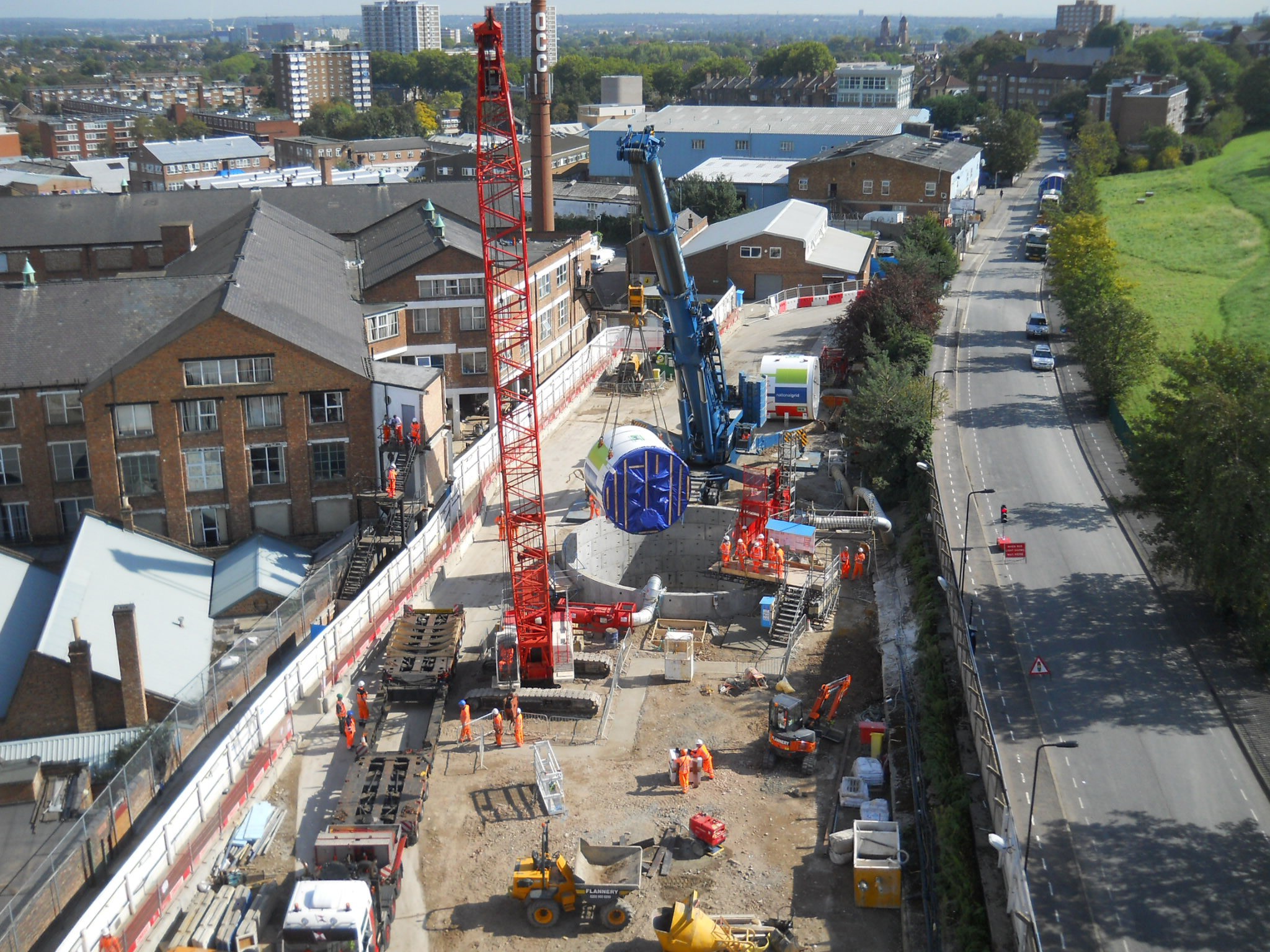 London Power Tunnels Vista aérea de un concurrido sitio de construcción con grúas y trabajadores en un entorno urbano cerca de una carretera.