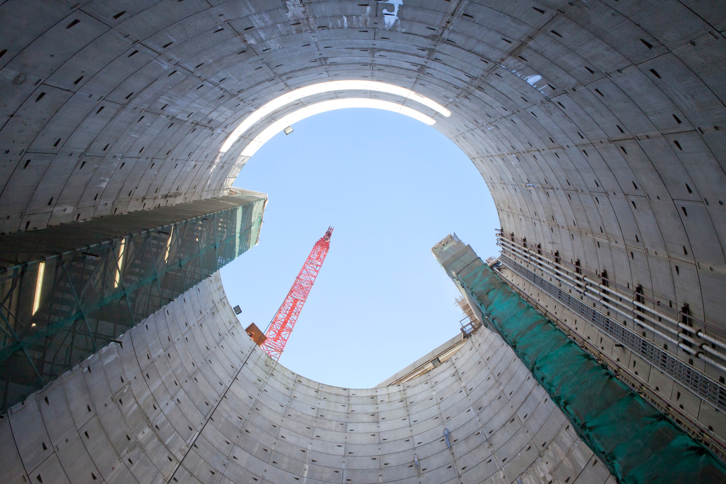 View from inside a large construction shaft with a visible crane and blue sky overhead.