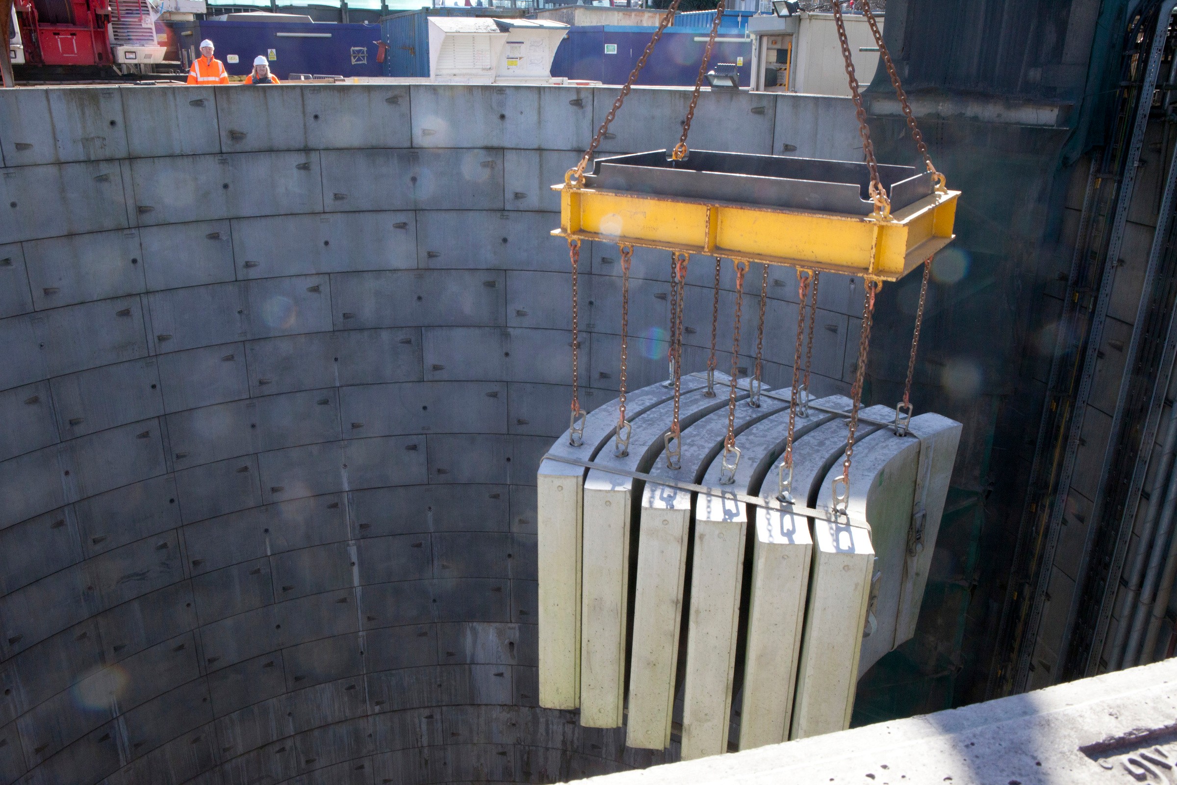 London Power Tunnels Concrete panels being lowered into a large circular construction pit using a crane.