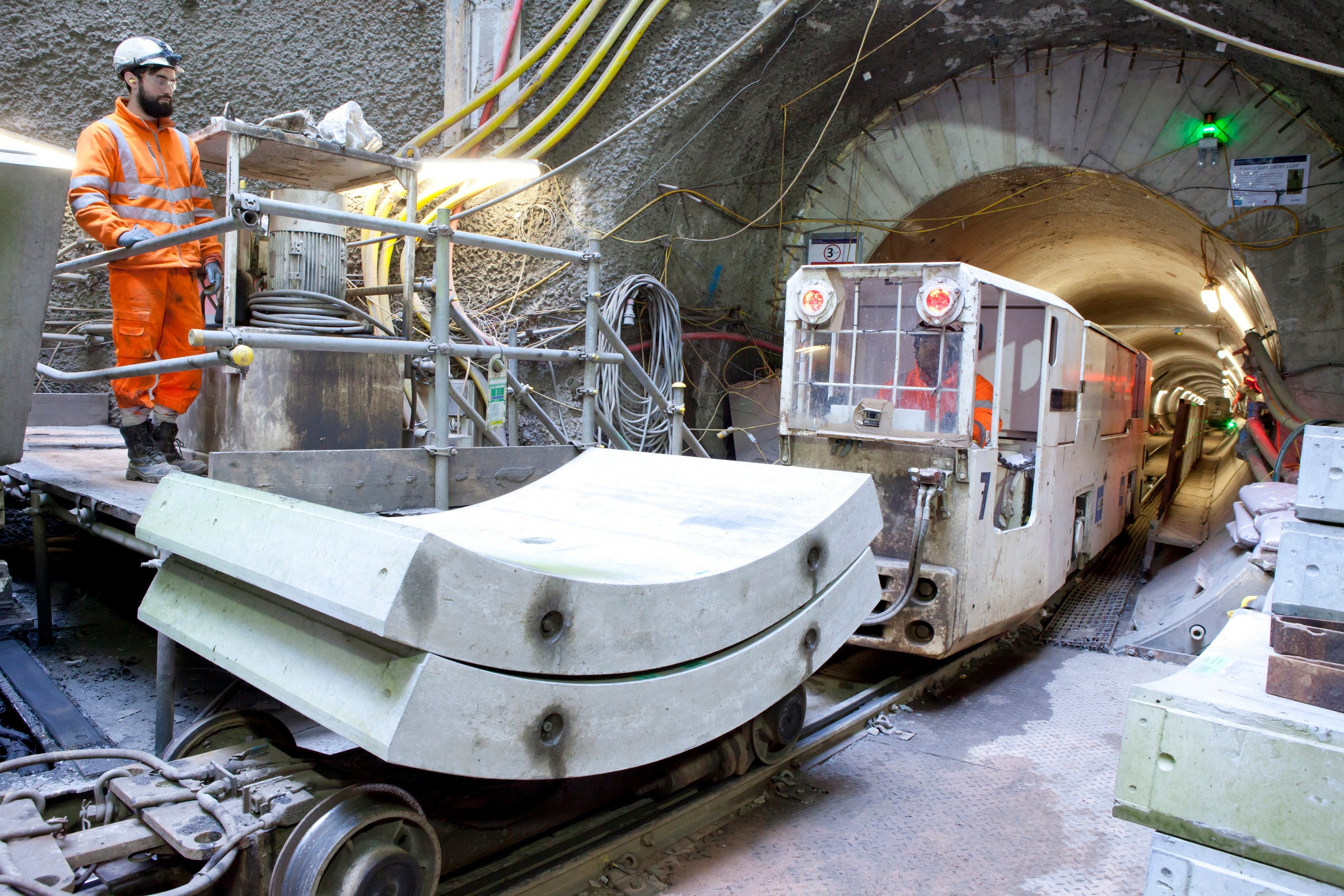 Construction worker operates machinery in a tunnel with a transport vehicle and concrete segments.