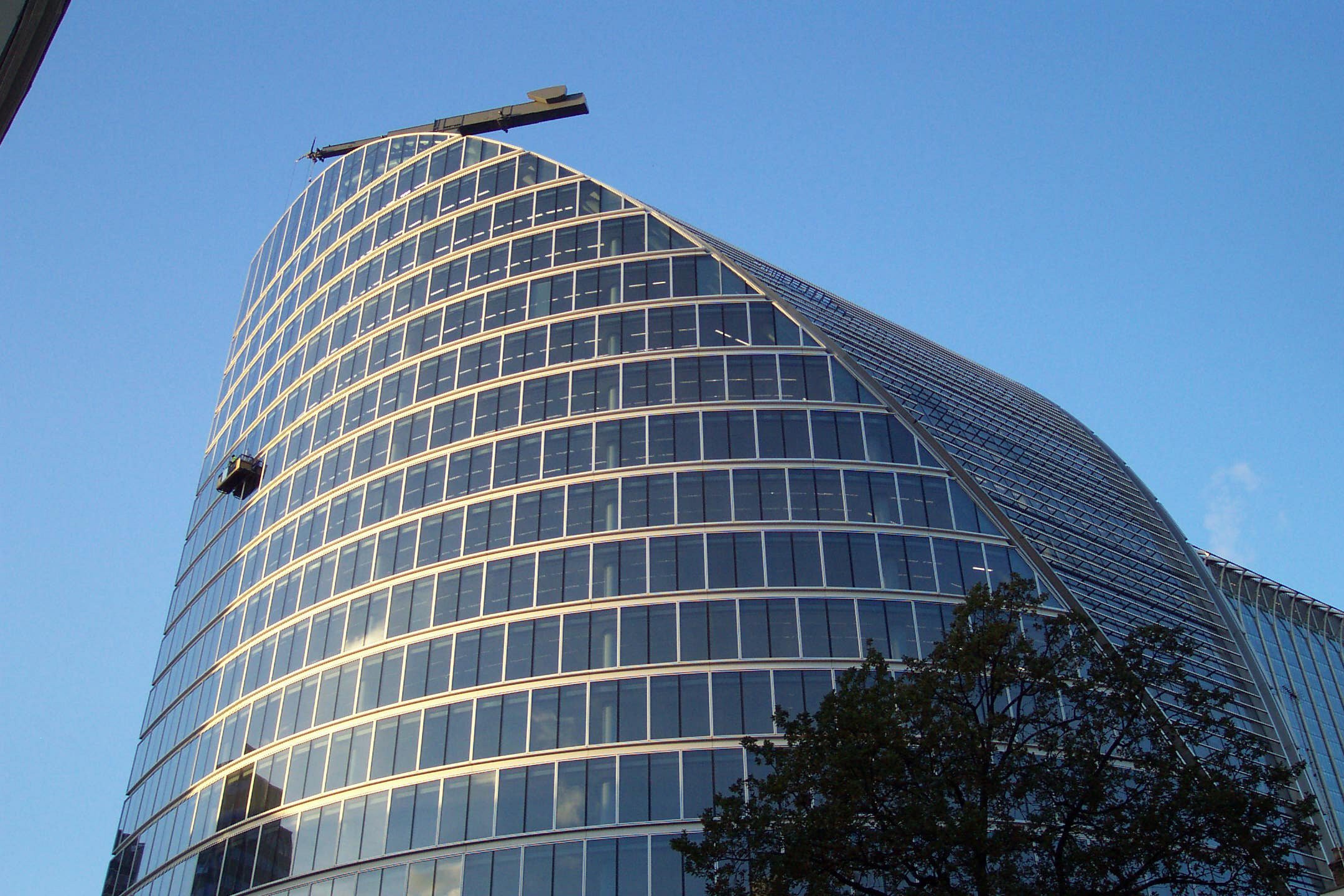 Modern curved glass skyscraper with reflective windows against a clear blue sky.