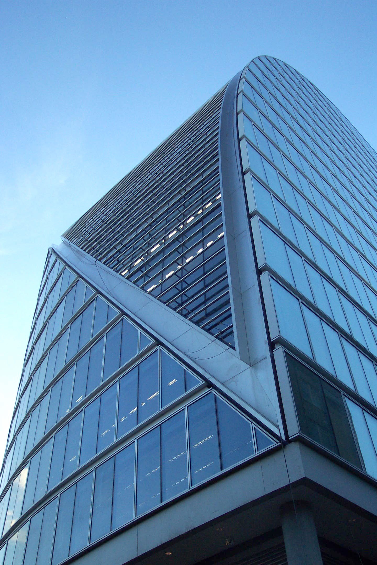 Moderne Glasbürogebäude mit geschwungener Struktur vor klarem blauem Himmel.