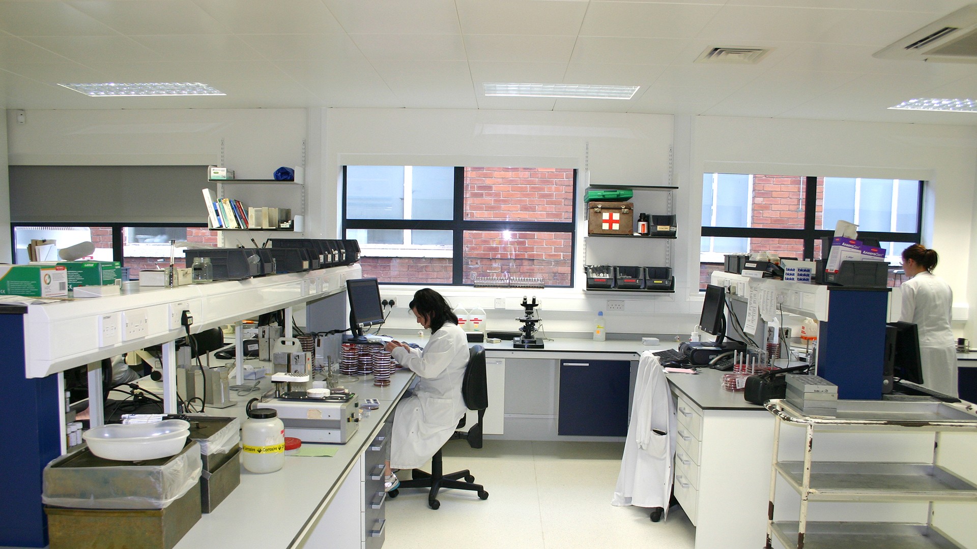 Modern laboratory with researchers working at computers and equipment, featuring large windows.