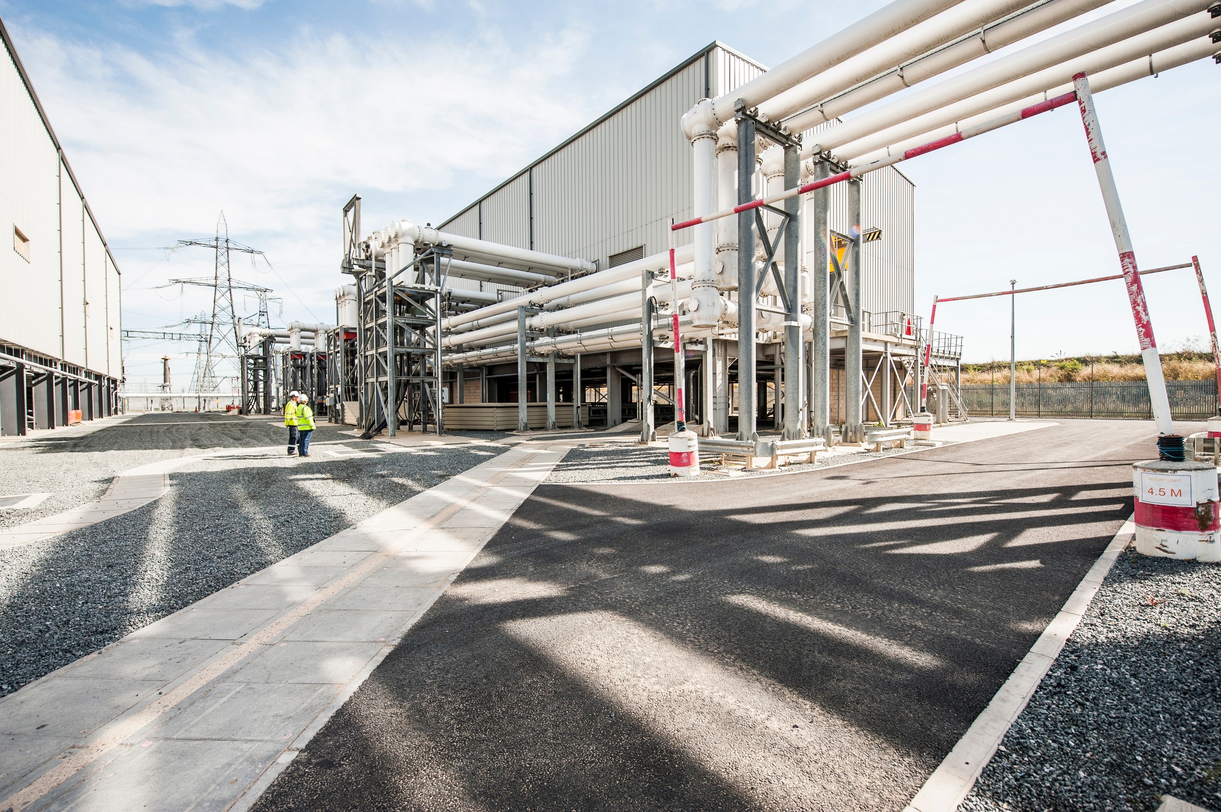 Modern Industrial Facility with Extensive Piping System Industrial facility with extensive piping and a worker in protective gear, under clear skies.