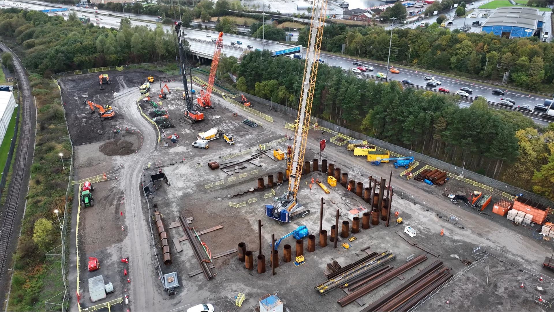 Aerial view of a construction site with cranes, heavy machinery, and steel piles in progress.