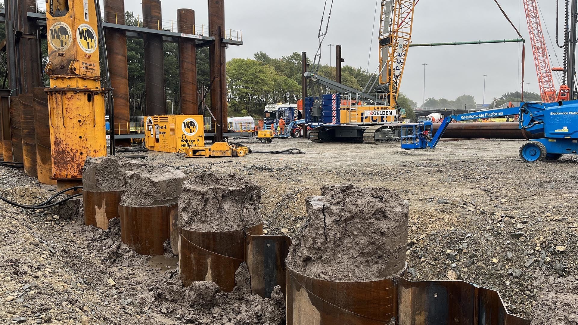 Construction site with heavy machinery, metal piles, and soil in an industrial setting.