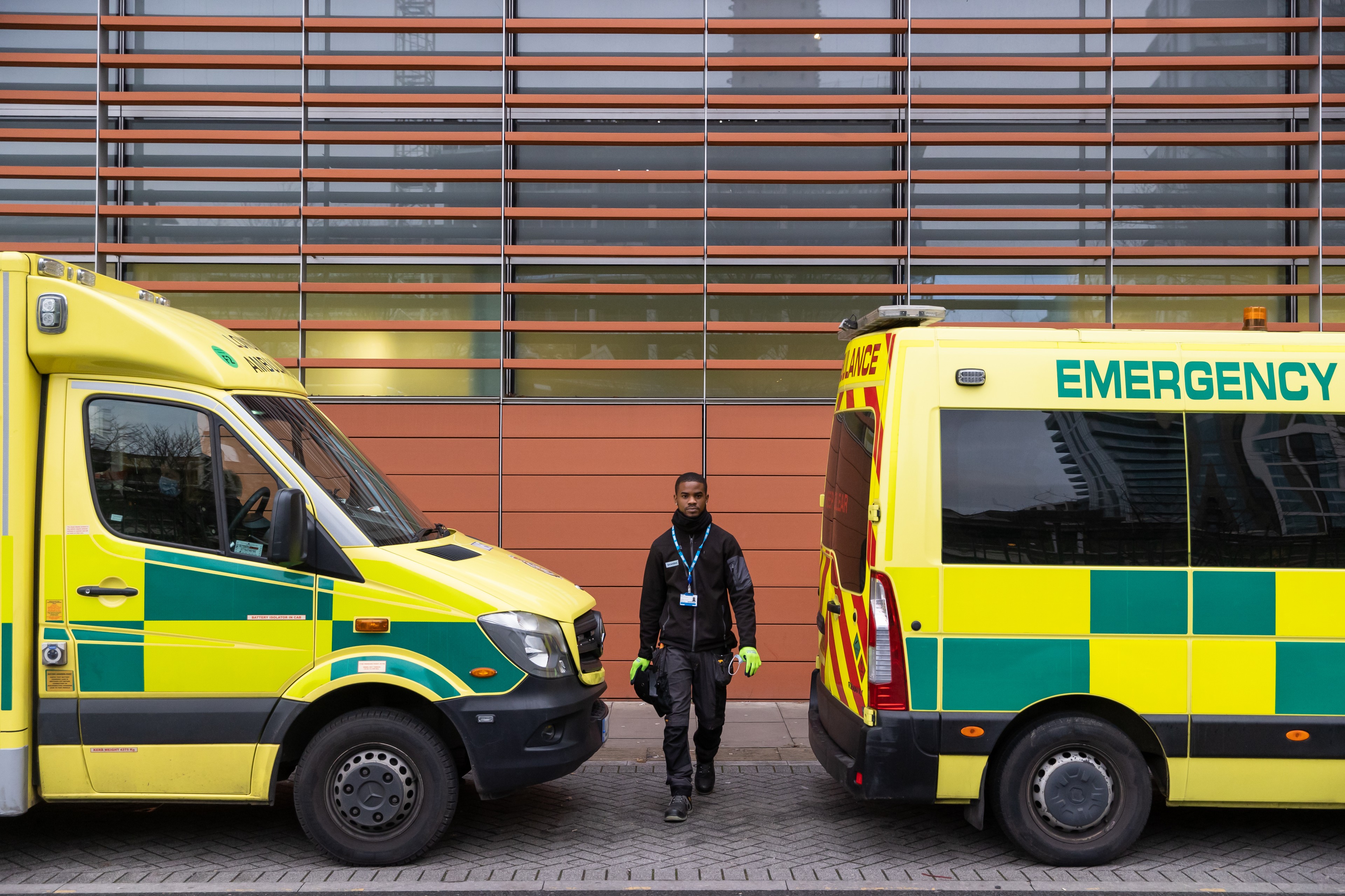 Barts and Royal London Hospital, built by Skanksa UK A person stands between two yellow and green emergency vehicles parked outside a modern building.