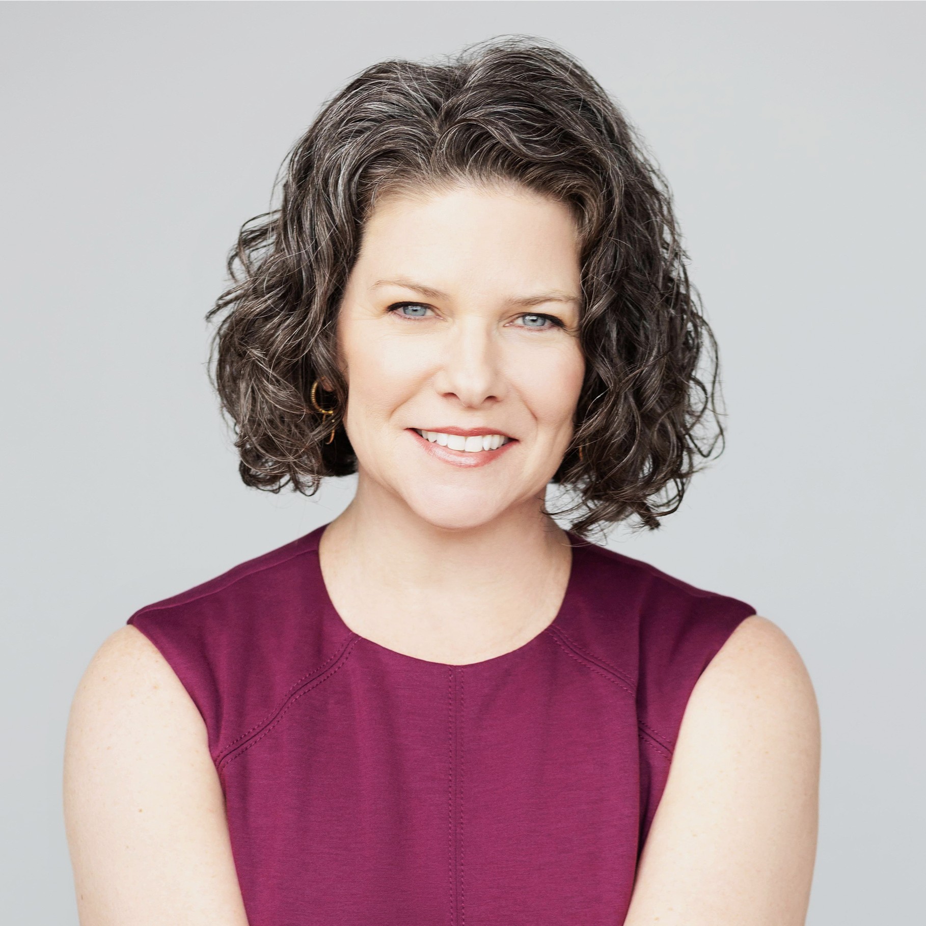 Professional woman with short curly brown hair wearing a sleeveless maroon top.