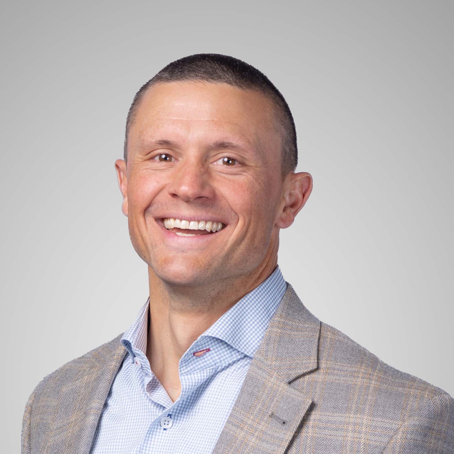 Brian Bozeman a gray plaid suit jacket and checkered blue shirt, posed against a neutral background.