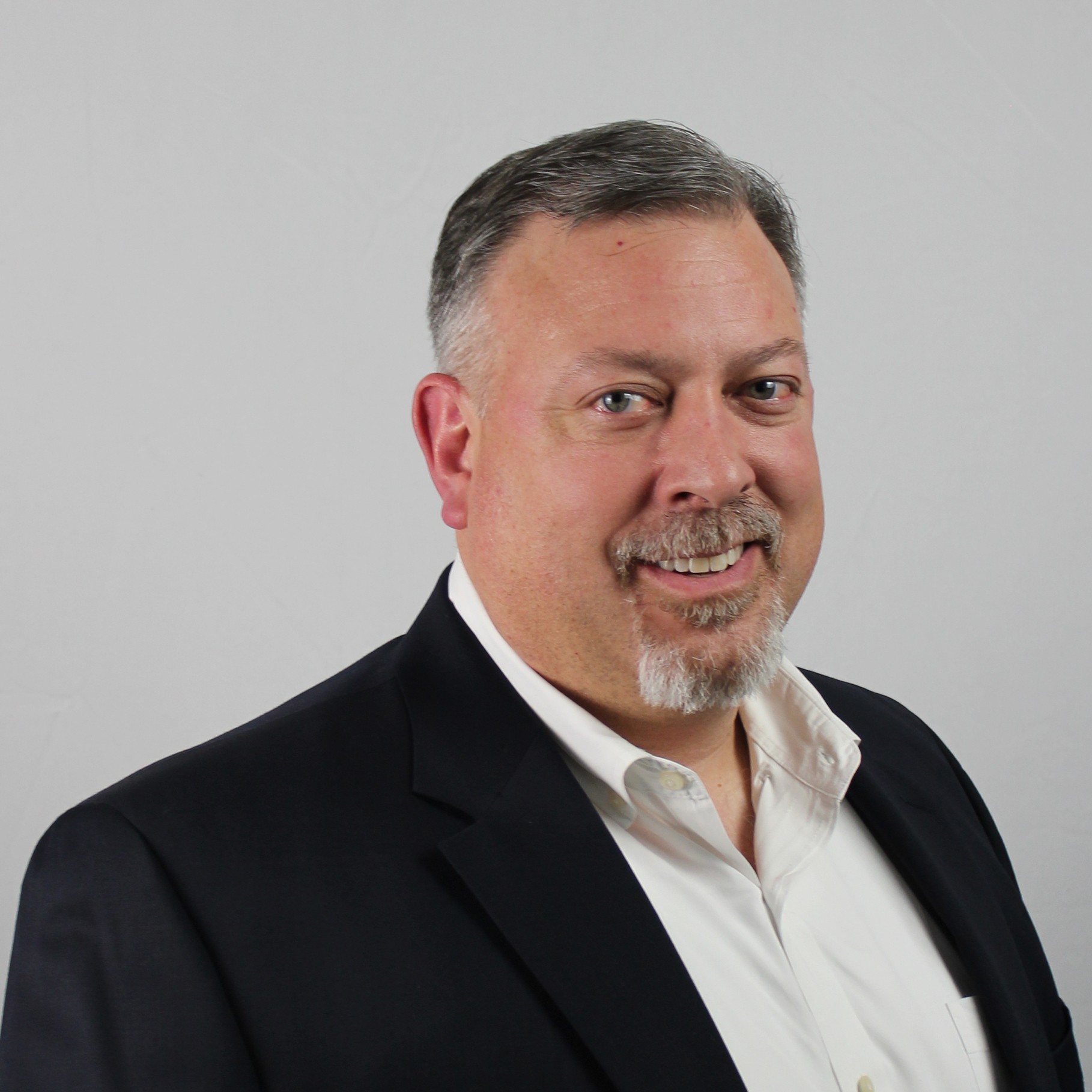 A person in a black suit and white shirt against a neutral background.