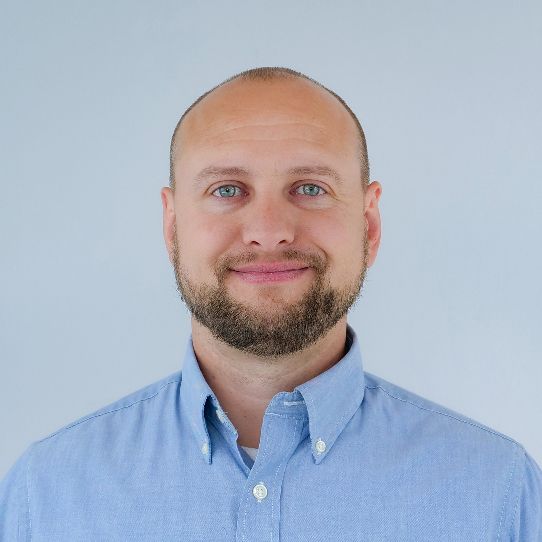 Man Wearing Blue Button-Down Shirt Against Gray Background A man wearing a light blue button-up shirt stands against a plain gray background.