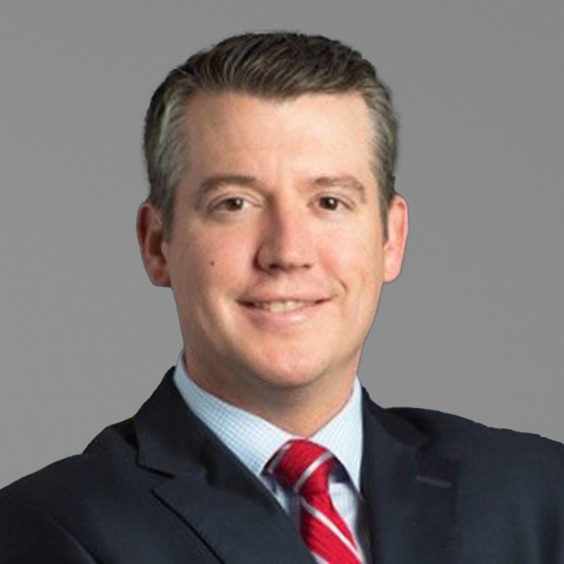 Professional Portrait in Suit and Tie Person wearing a dark suit jacket, white dress shirt, and red striped tie, seated against a dark background.