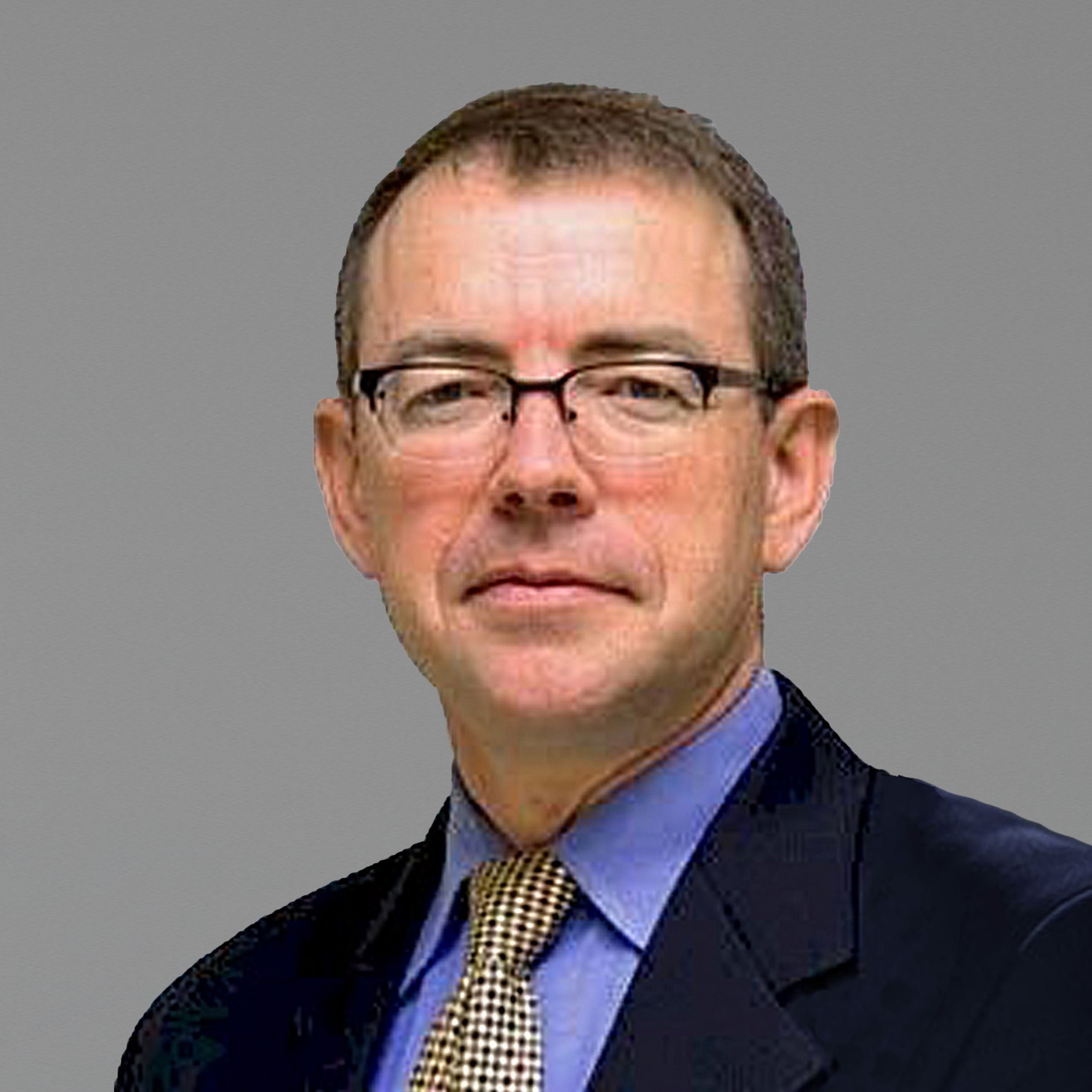 Professional businessman in suit and tie on gray background Andrew wearing a dark suit, blue shirt, and patterned tie against gray.