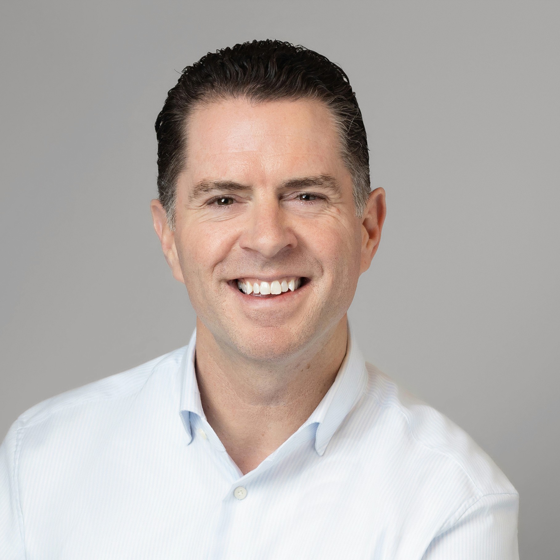 Man wearing a white button-up shirt with dark hair against a plain gray background.