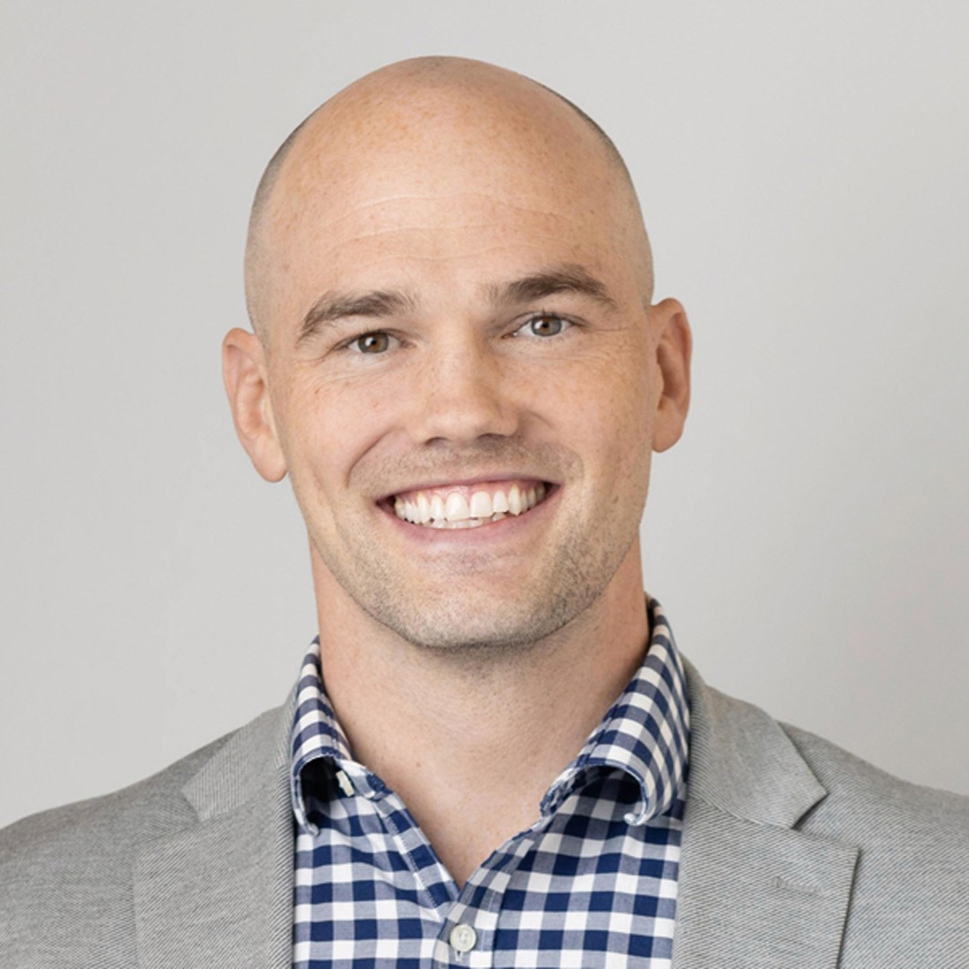 Bald Man Wearing Gray Blazer and Checkered Shirt Portrait Professional man wearing a gray blazer and blue checkered shirt against a plain background.