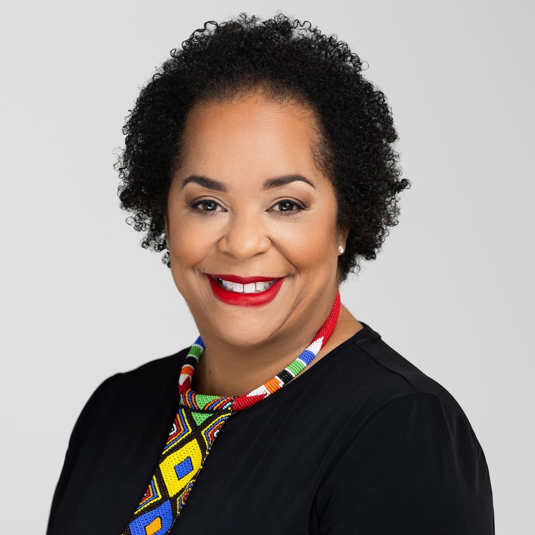 Colorful Beaded Necklace with Curly Hair and Black Outfit Woman wearing a colorful beaded necklace and black top against a plain gray background.