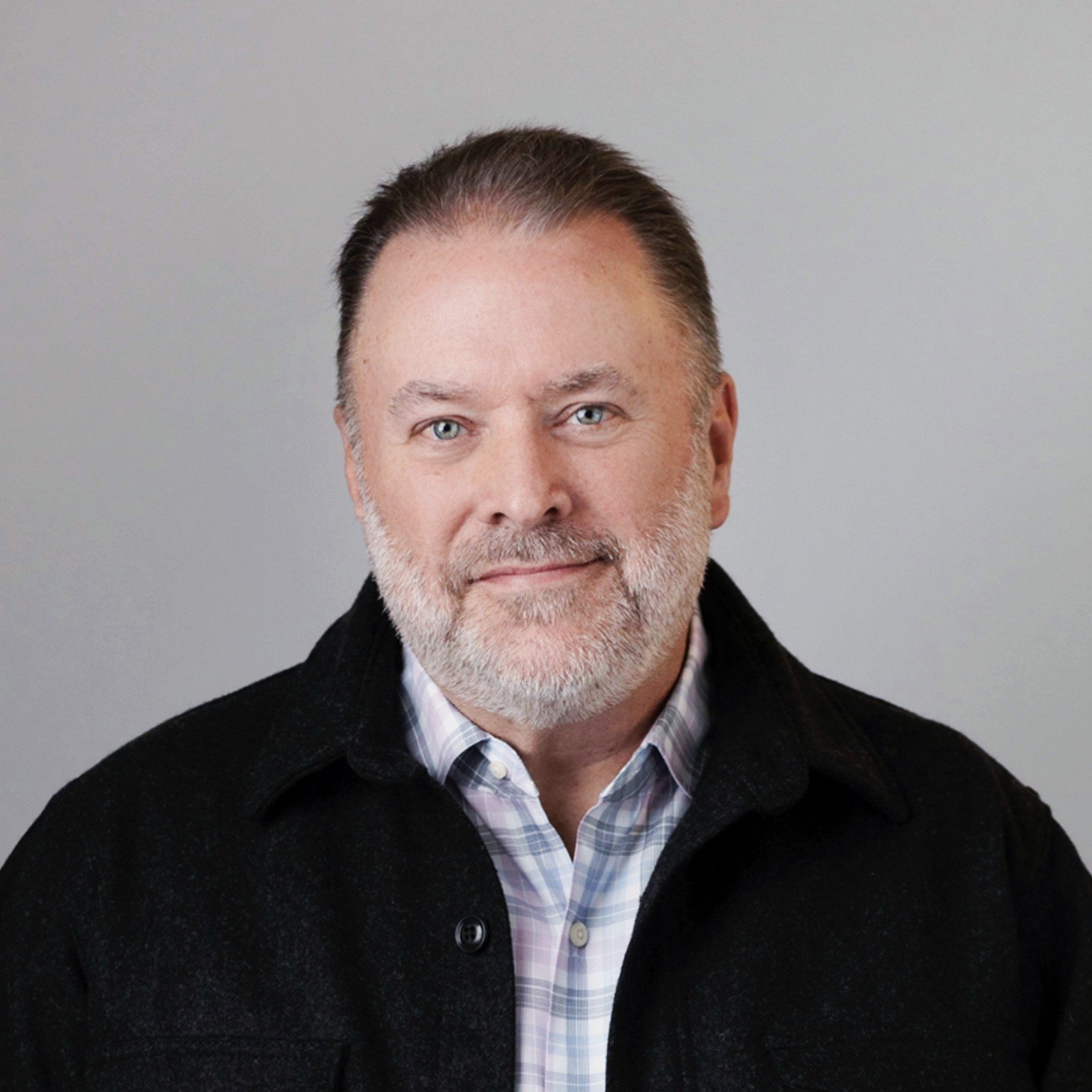 Mature Man Wearing Black Jacket and Plaid Shirt on Gray Background Middle-aged man wearing a black jacket and plaid shirt against a plain gray background.