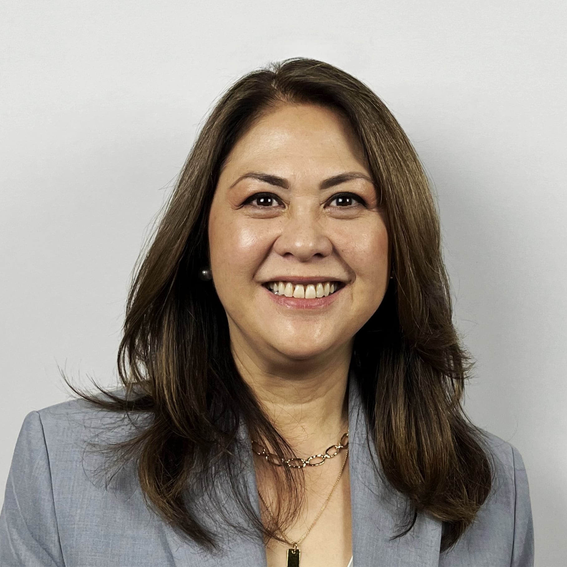Professional woman in grey blazer with layered brown hair Professional woman with shoulder-length brown hair wearing a gray blazer and necklaces.