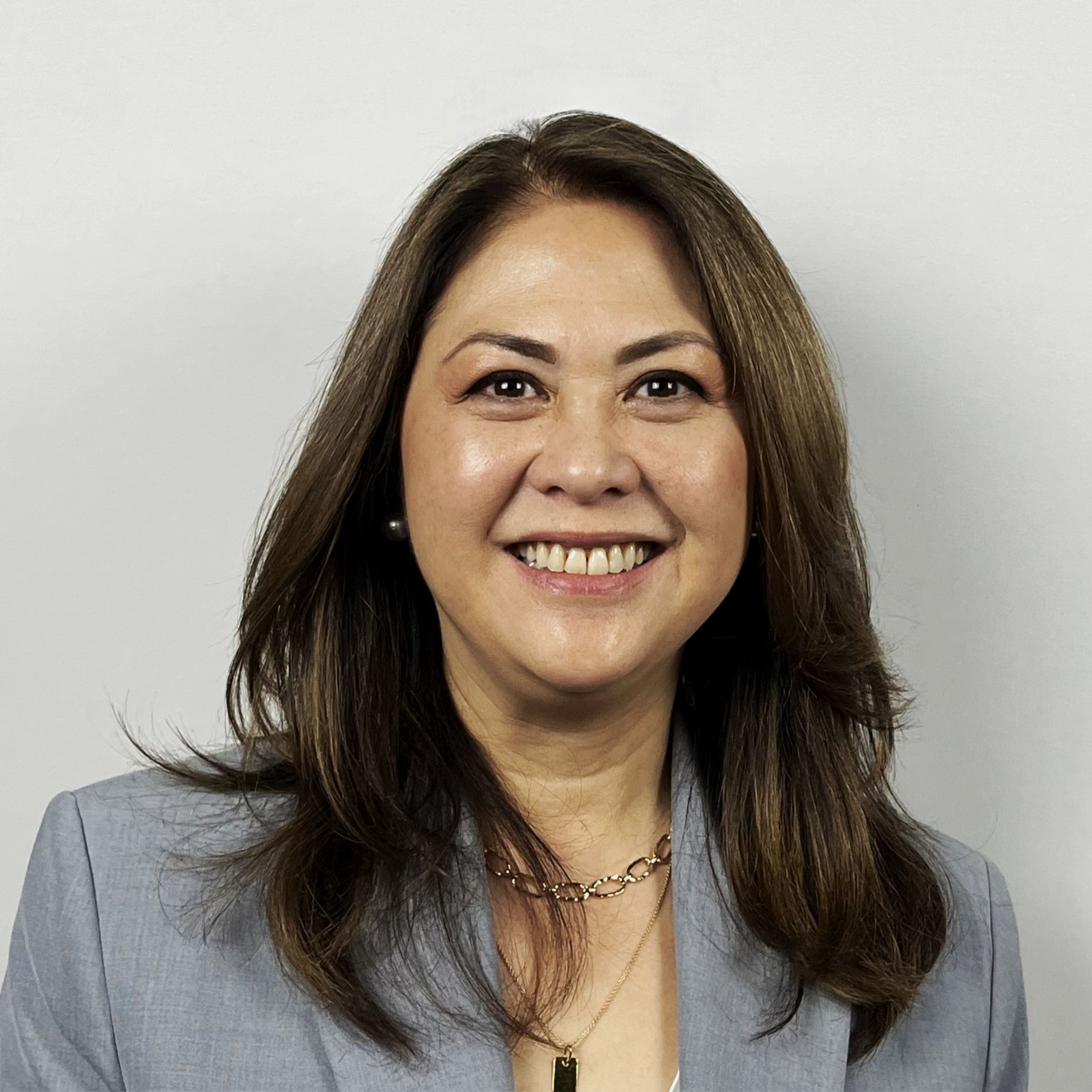 Professional woman with shoulder-length brown hair wearing a gray blazer and necklaces.