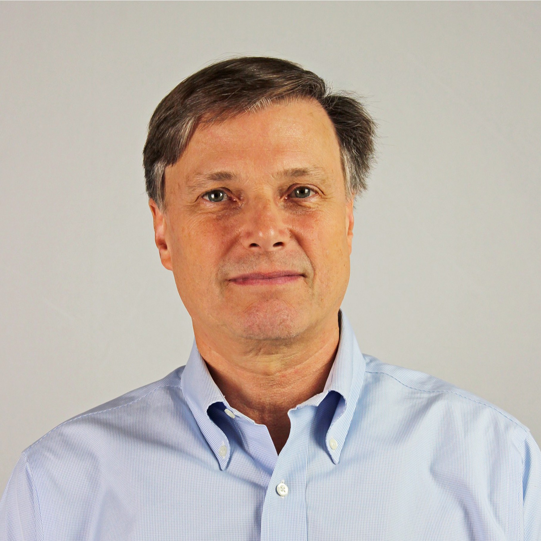 A man in a blue button-down shirt poses against a neutral gray background.