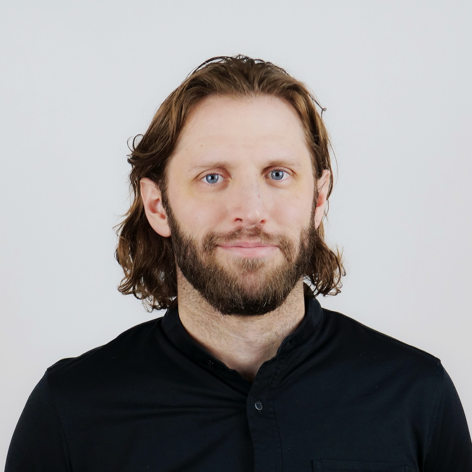 Man with medium-length brown hair wearing a black button-up shirt against a gray background.