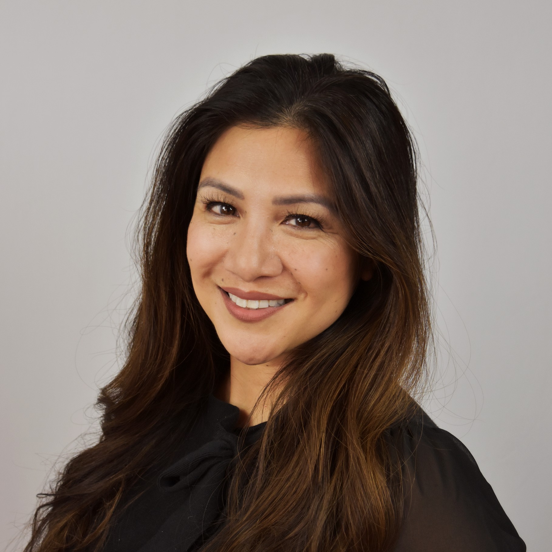 Portrait of a woman with long brown hair wearing a black top against a plain background.