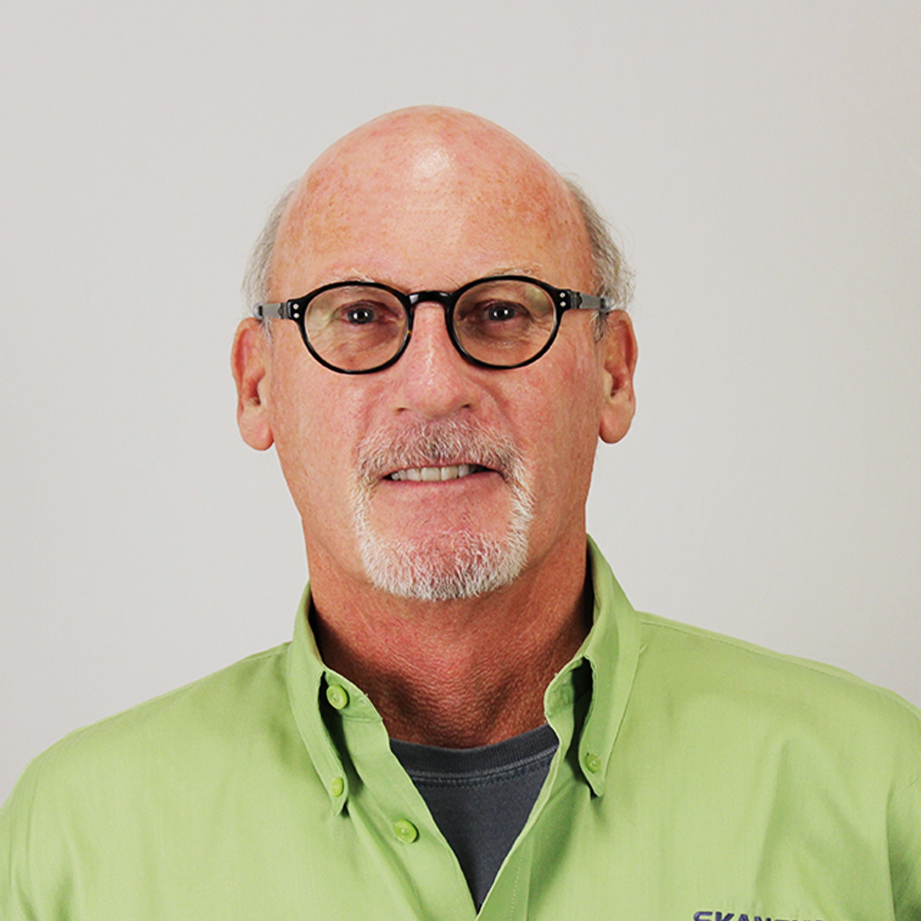 Man in Green Shirt with Company Logo - Professional Portrait A person wearing a light green Skanska shirt against a plain background.